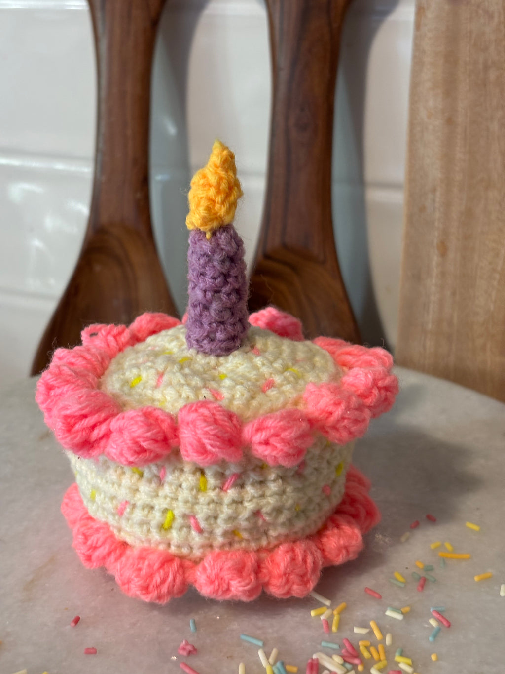 Crocheted birthday cake with a candle on a wooden chair.