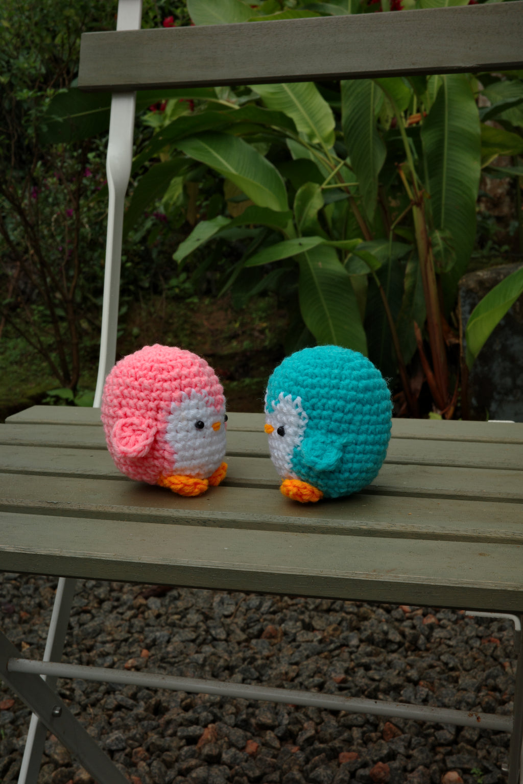 Two colorful crocheted bird balls on a wooden bench with greenery in the background