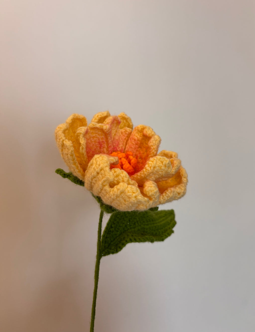 butter yellow crochet peony flower with a lush green leaf