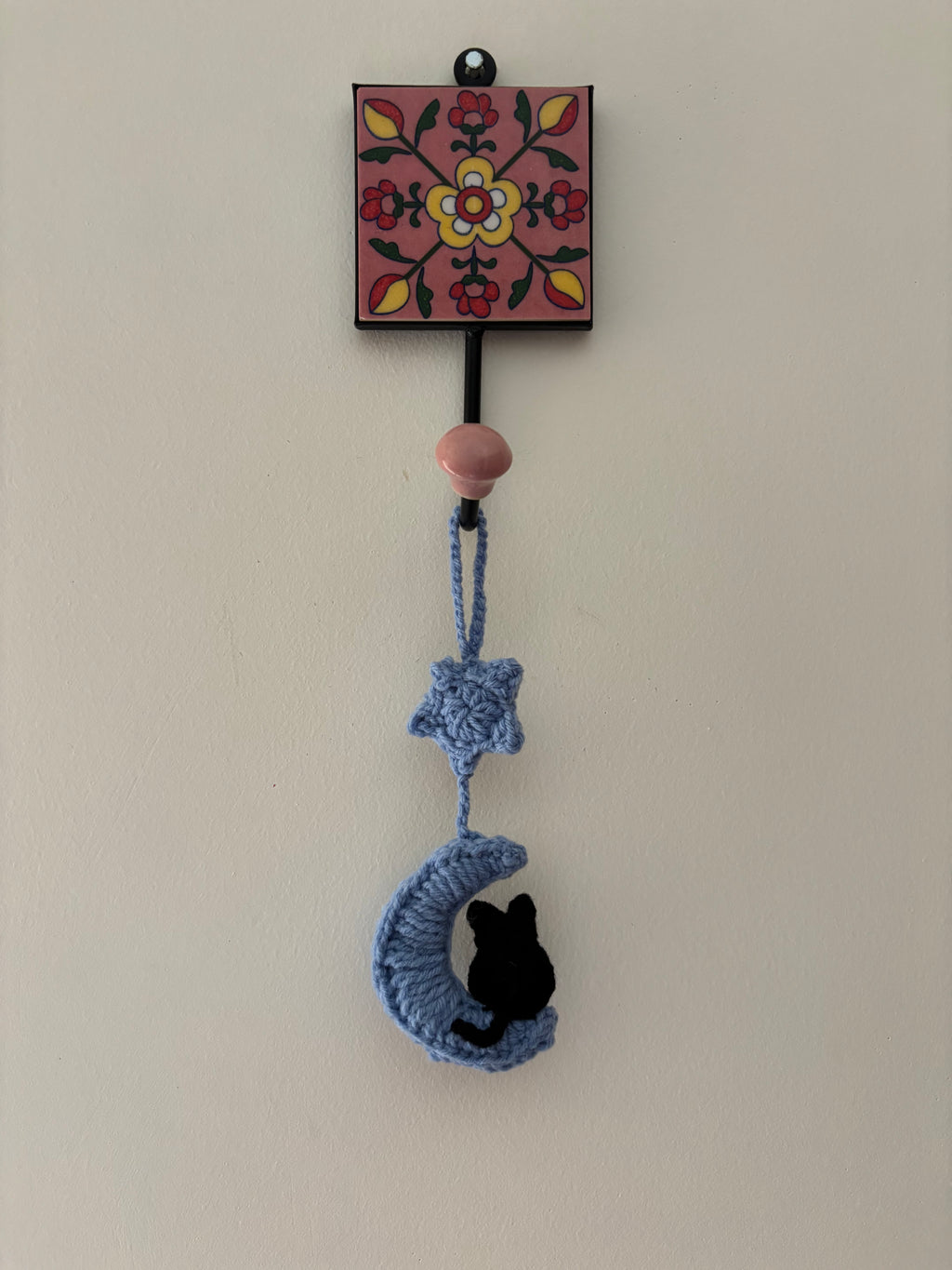 Decorative wall hook with floral design and crocheted moon and star hanging on a plain wall.