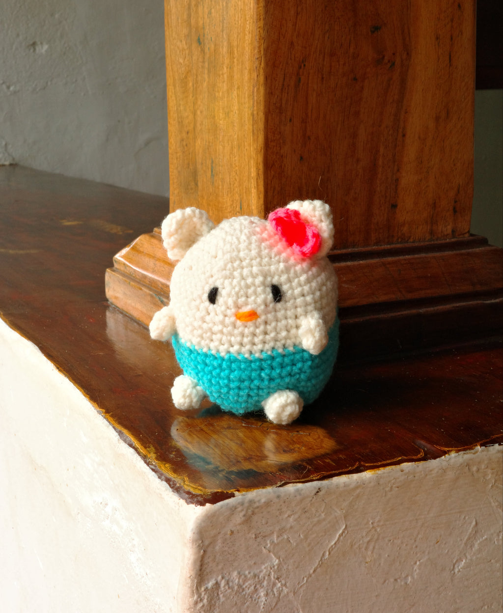 Small crocheted hello kitty figurine with a blue dress on a wooden surface
