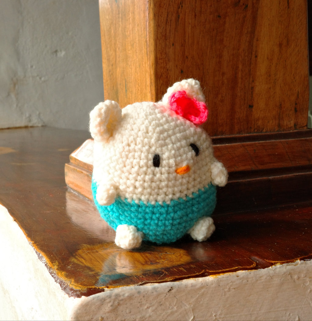 Small crocheted cat toy with a pink bow on a wooden surface