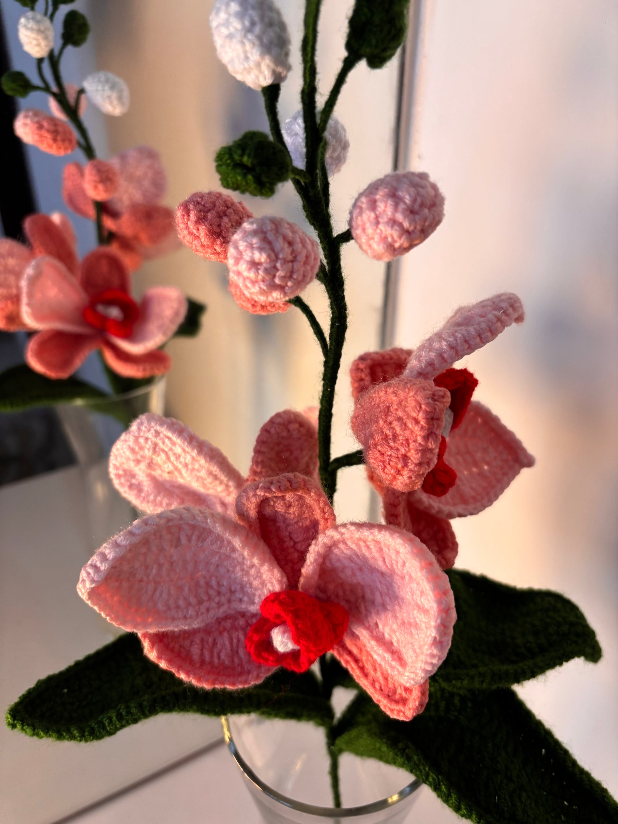 Knitted pink orchids with red centers in a clear vase against a blurred background