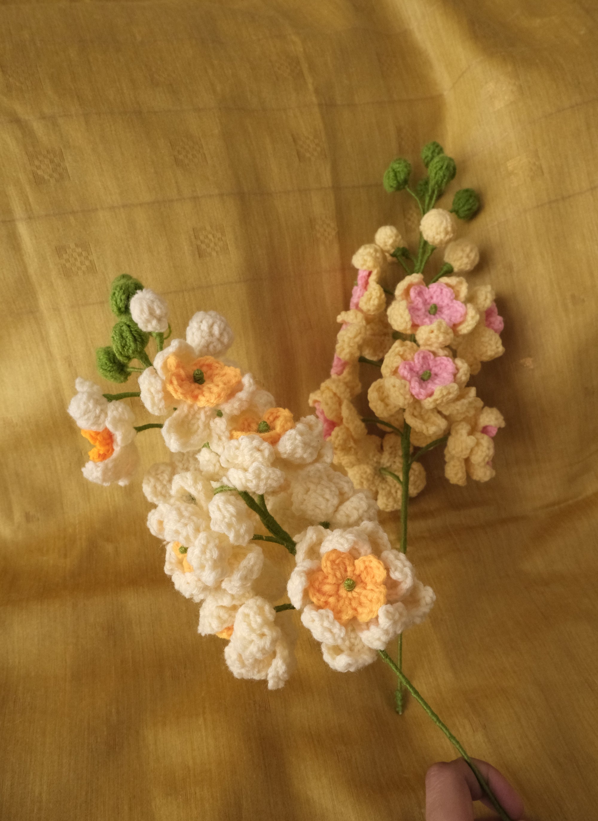 Handmade crocheted artificial flowers in cream, yellow, orange, and pink.