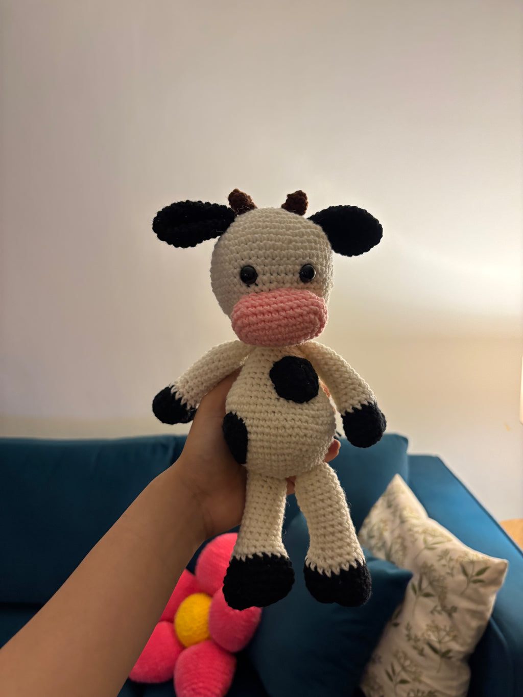 Hand holding a small crochet cow toy against a blue couch background