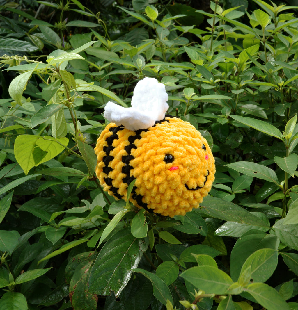 Crocheted bee toy with white wings on green leaves