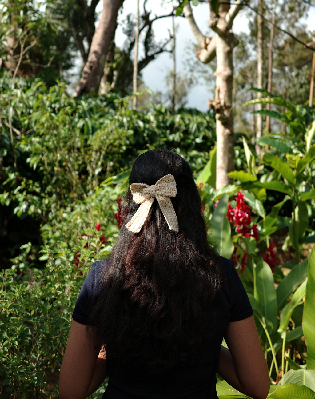 Person with a bow in their hair standing in a natural setting with trees and water.