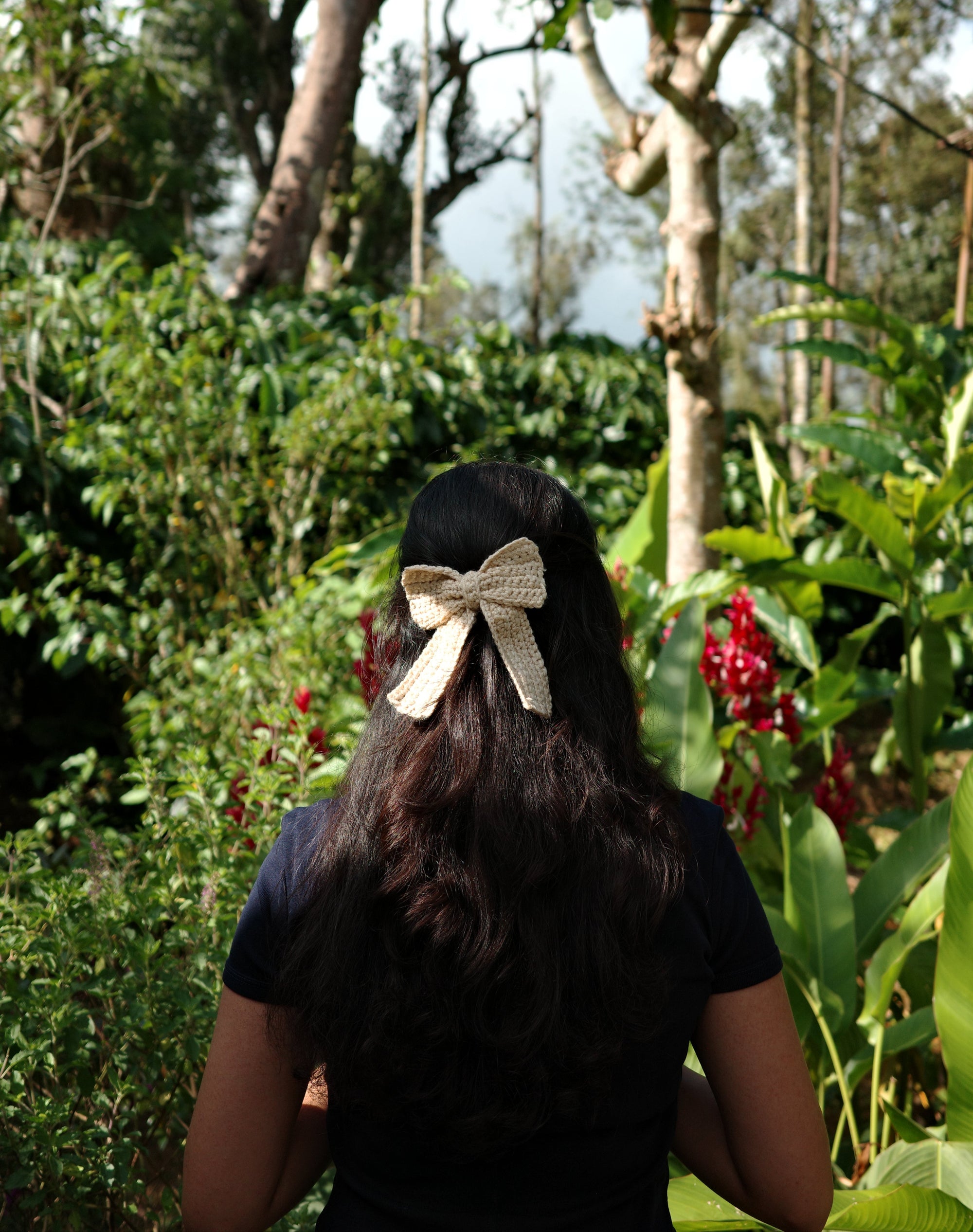 Person with a bow in their hair standing in a natural setting with trees and water.