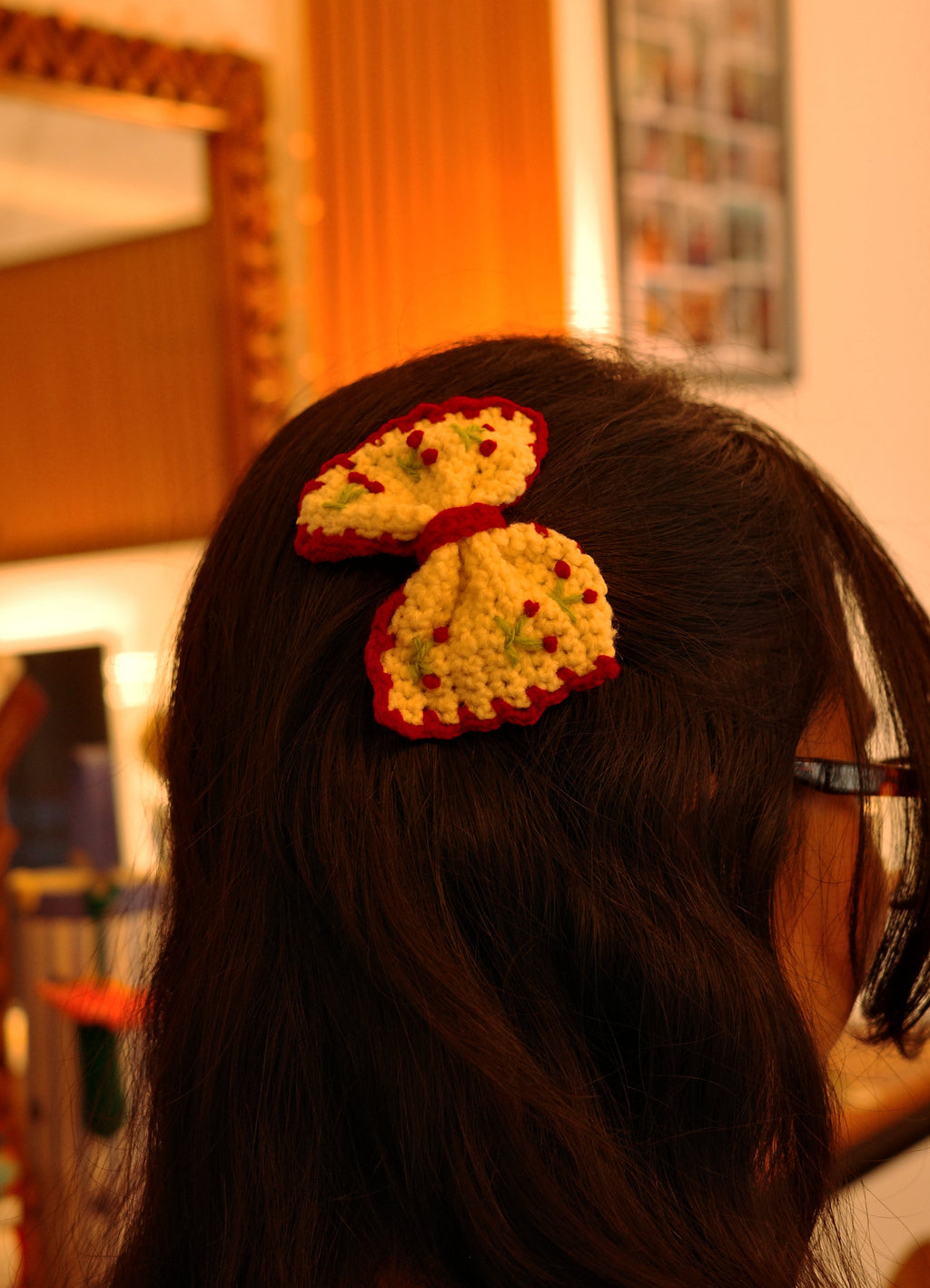 small handmade crochet cream bow with red border and tiny cherry details attached as a hair clip