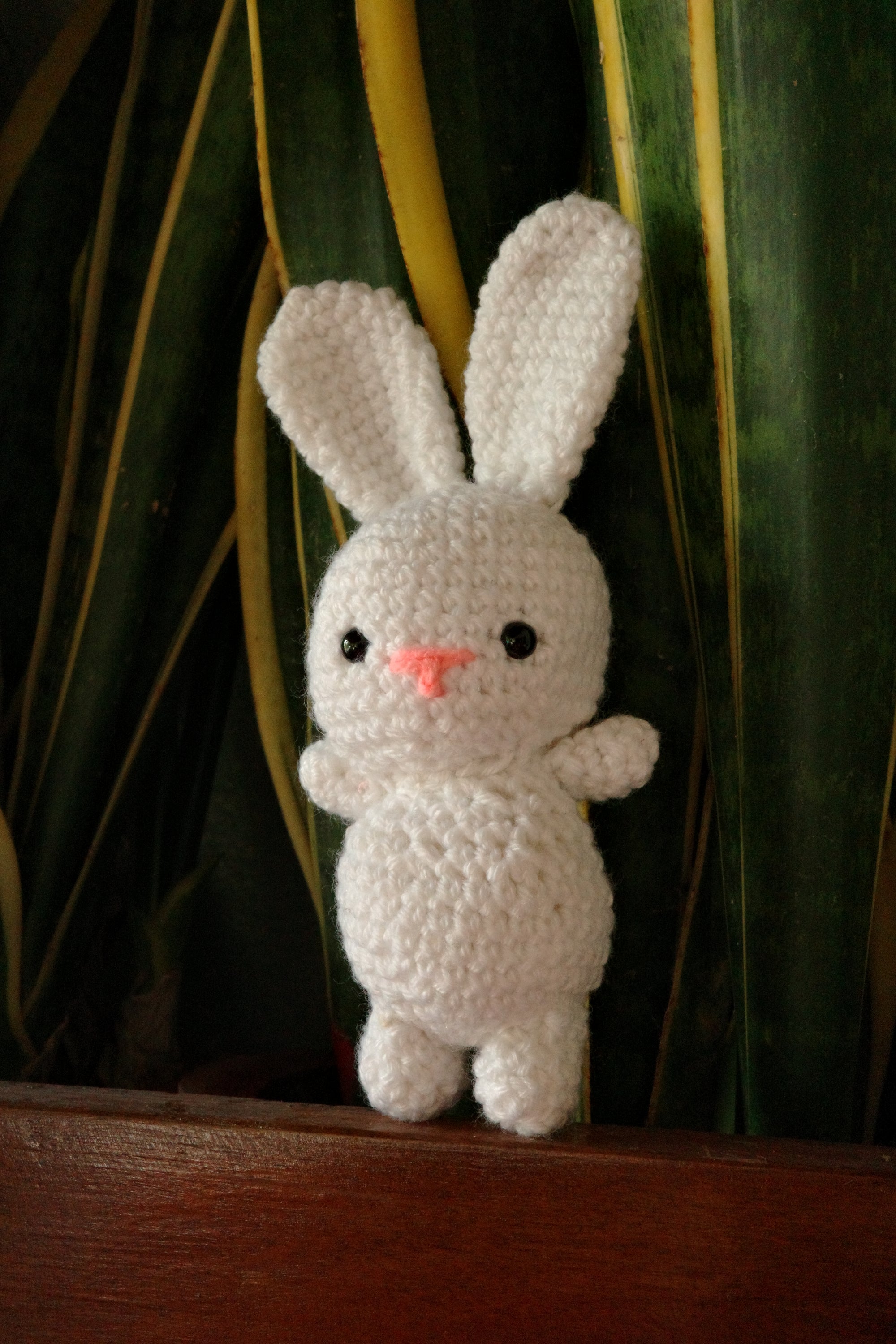 White crocheted bunny toy on a leafy background