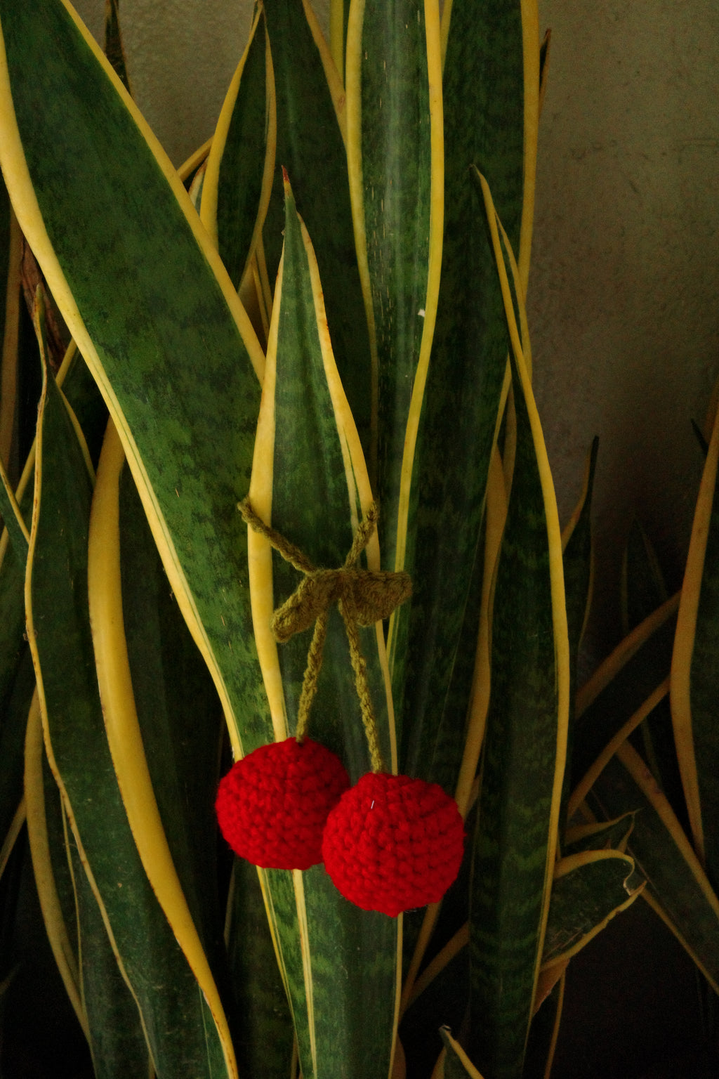 Two red crocheted berries on a green leaf with yellow veins