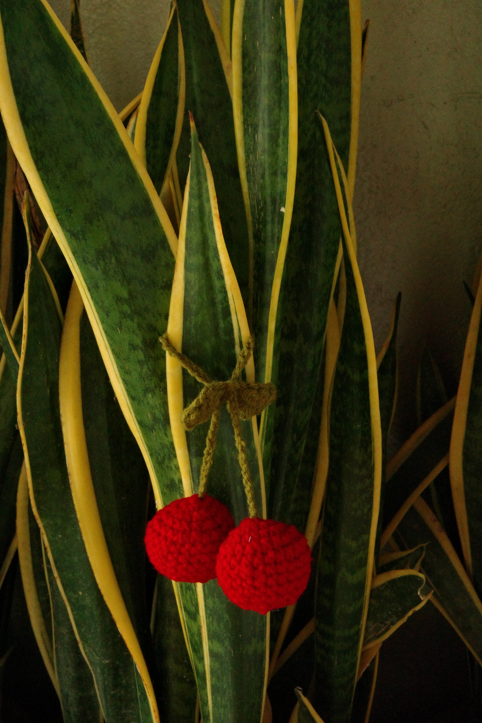 Two red crocheted berries on a green leaf with yellow veins