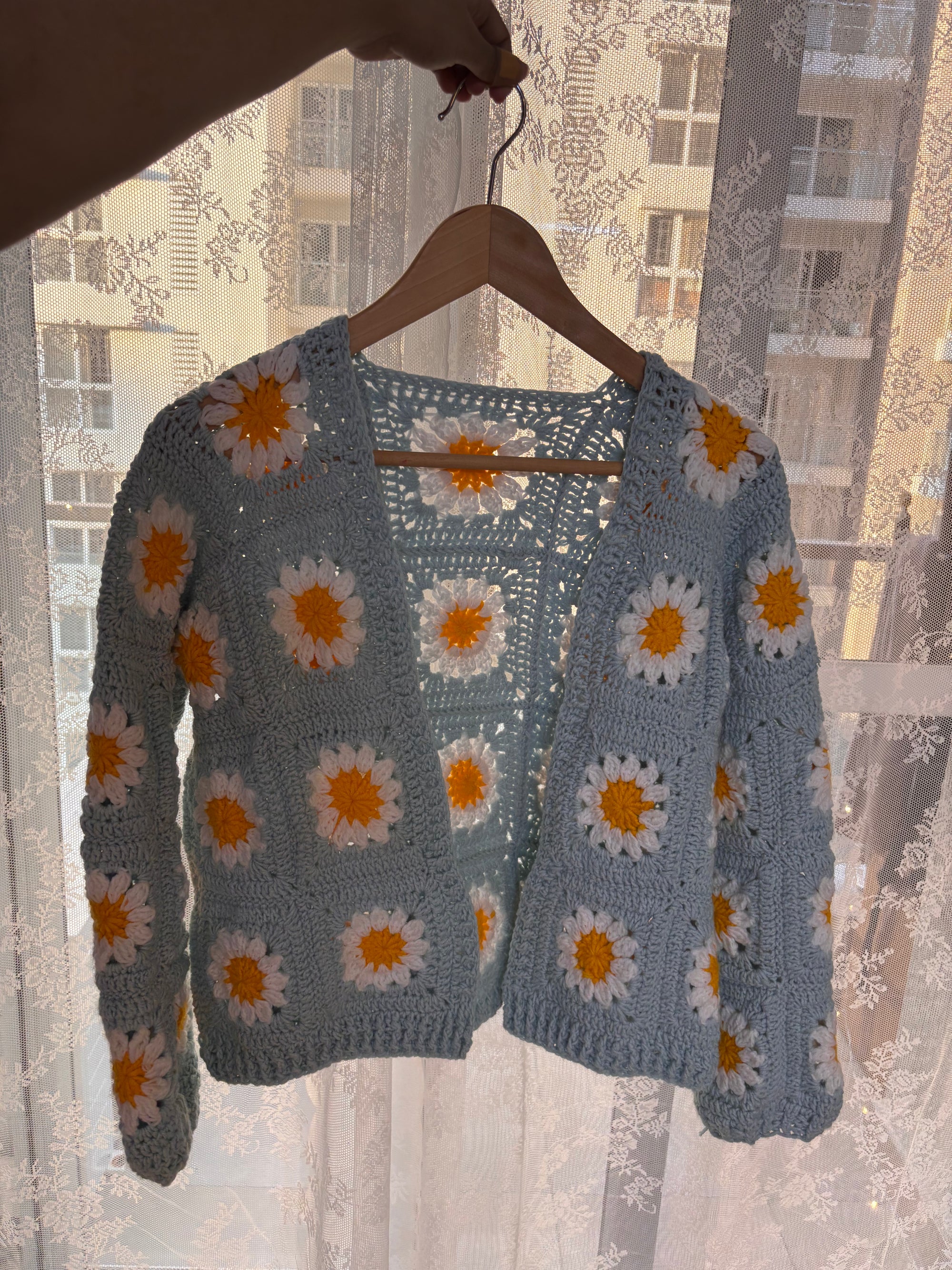 Crocheted cardigan with floral pattern on a hanger against a window backdrop
