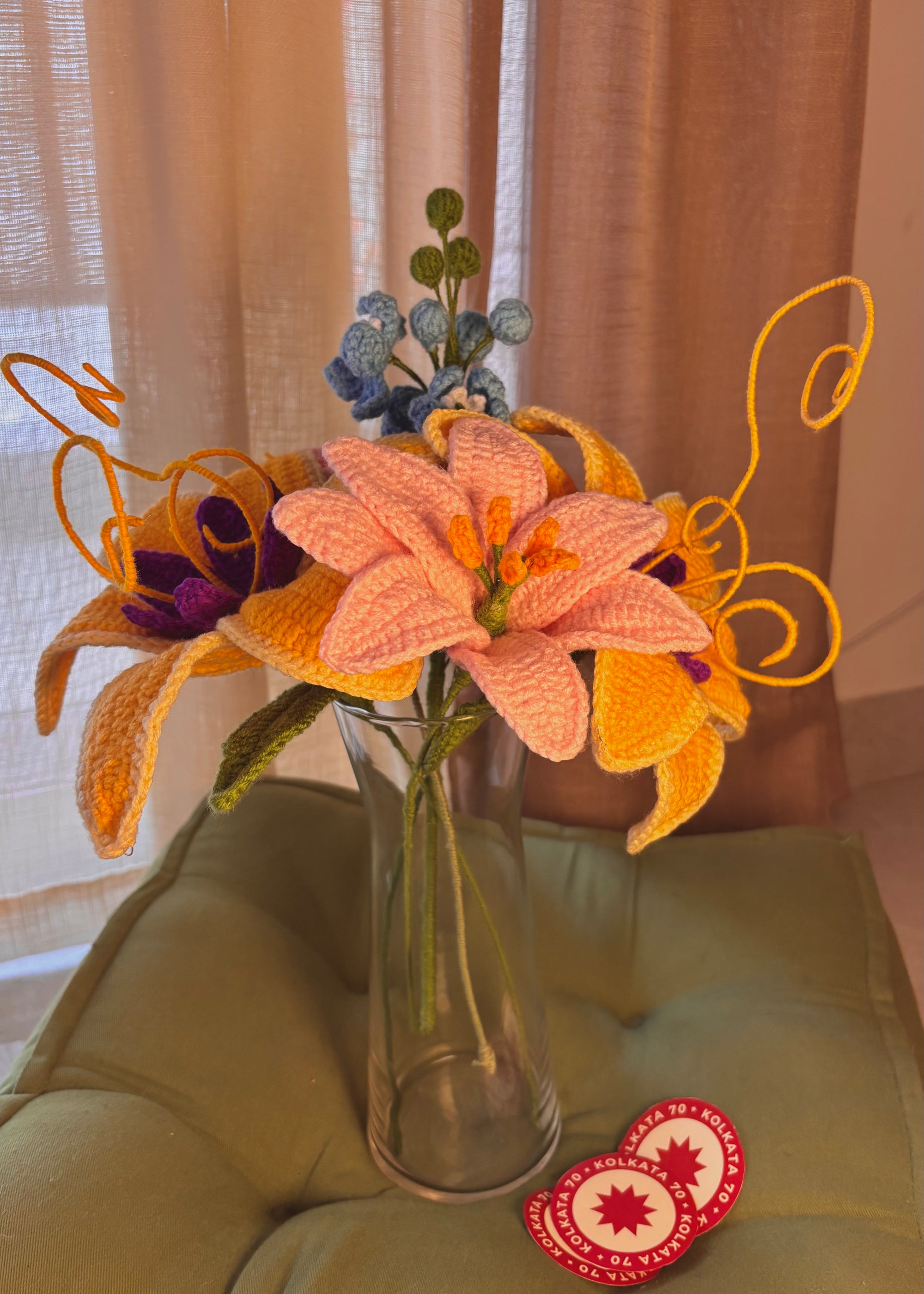 Knitted flowers in a clear vase on a green surface with a blurred background
