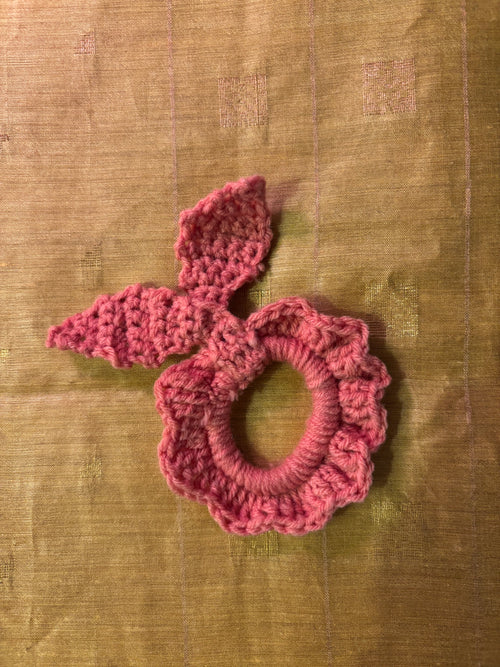 Pink knitted scrunchie with bow on a textured brown background