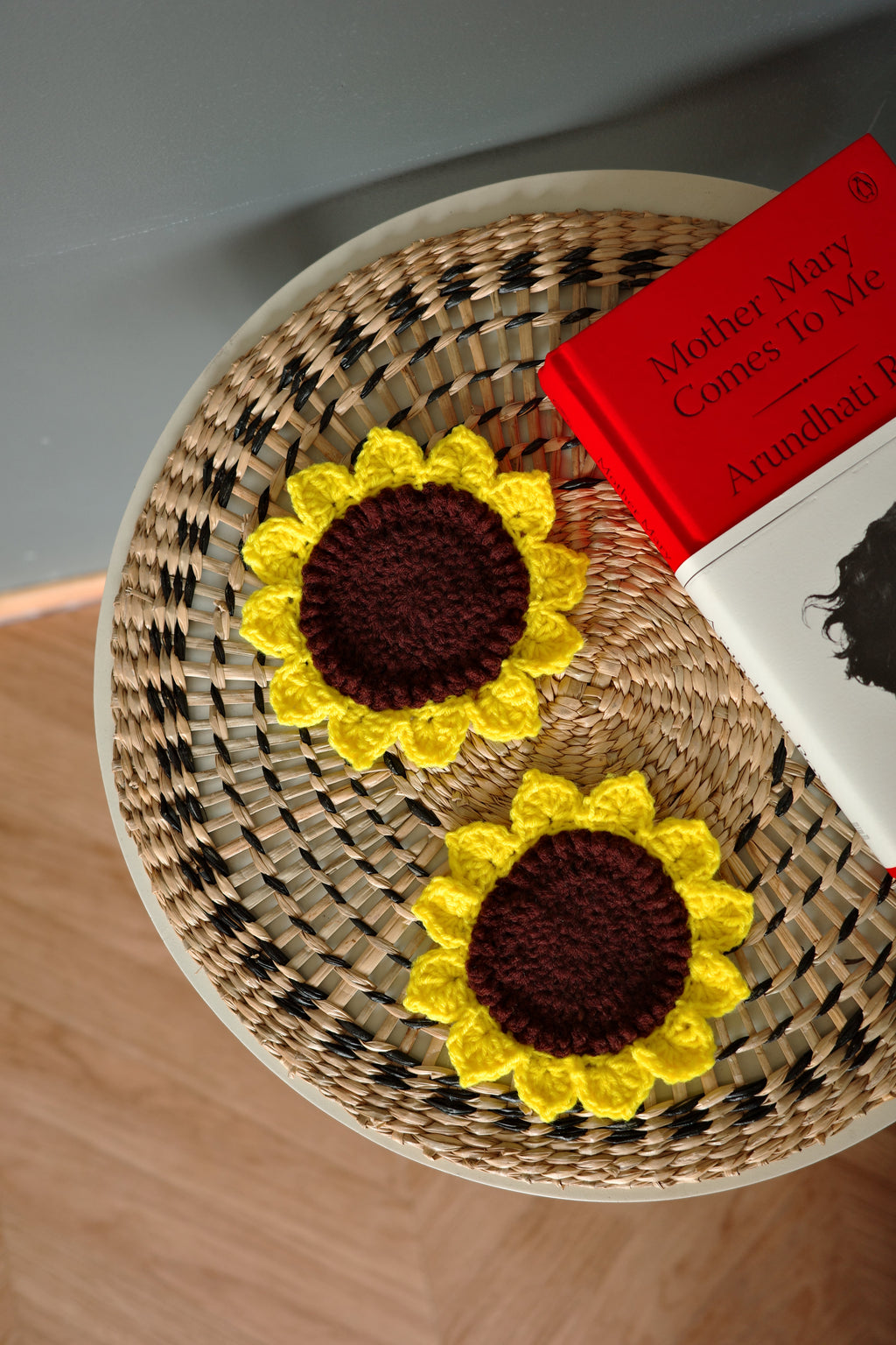 Two sunflower-shaped coasters on a woven surface with a book underneath.