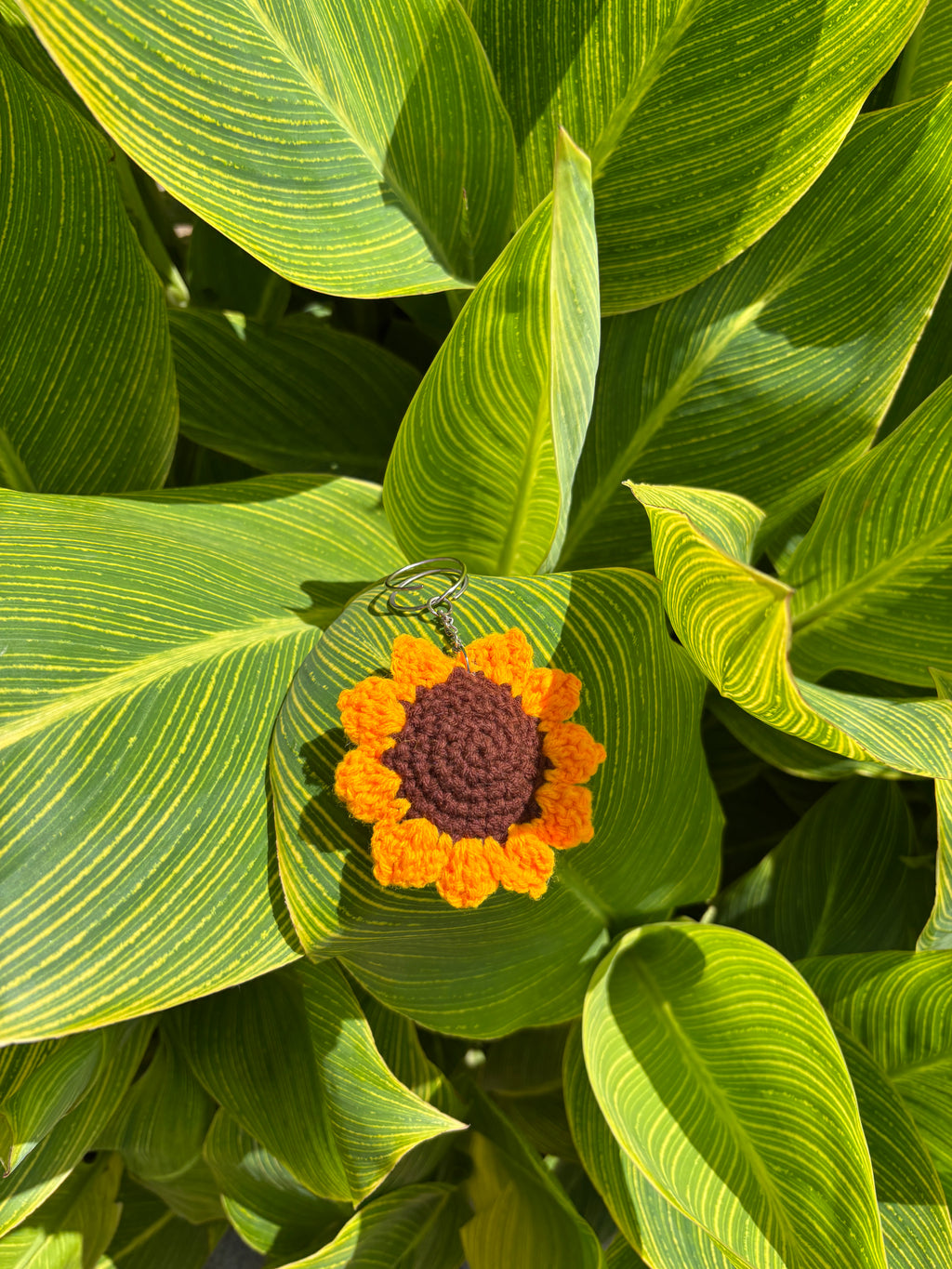 Crocheted sunflower keychain on a green leafy background
