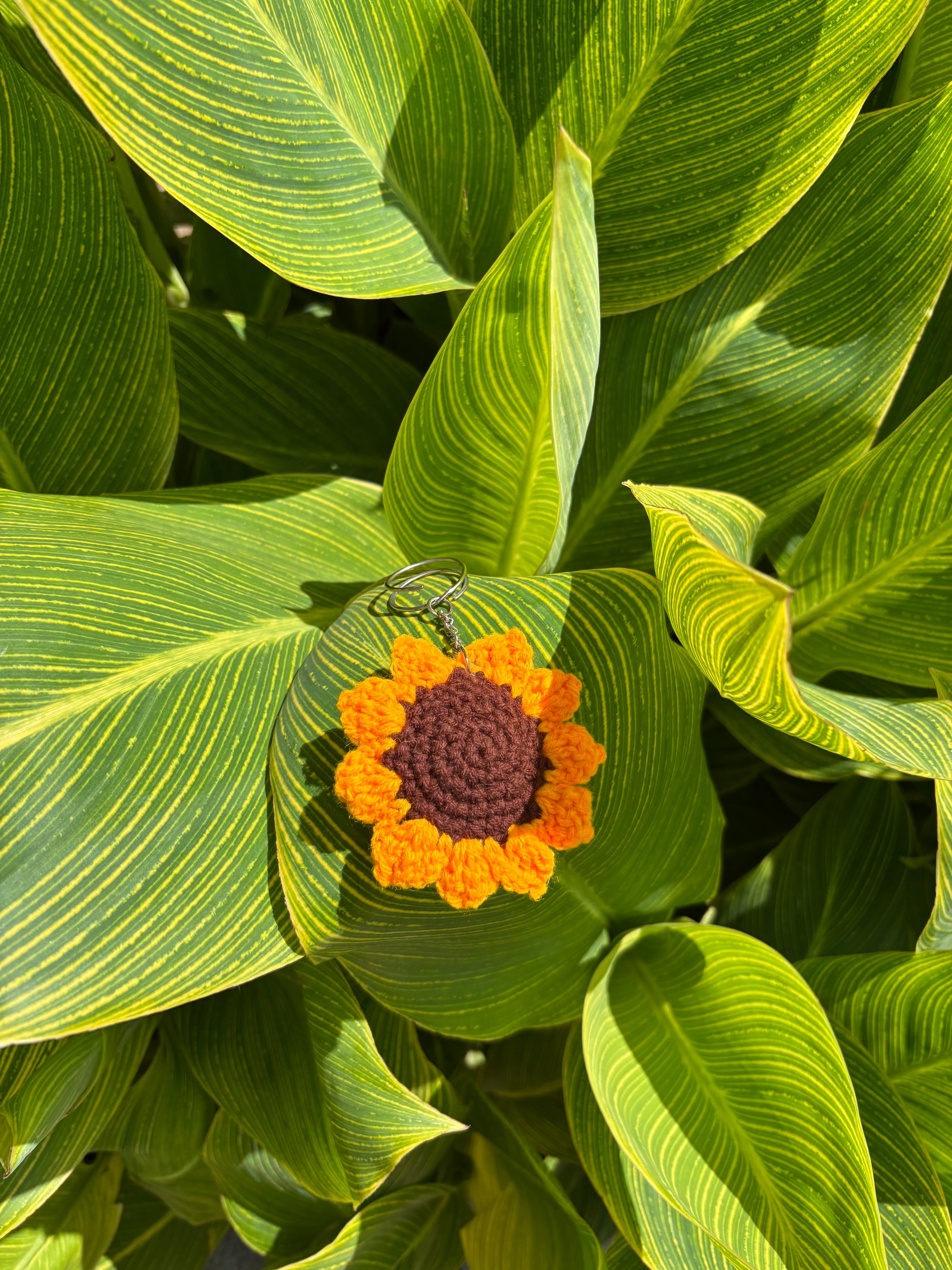Crocheted sunflower keychain on a green leafy background