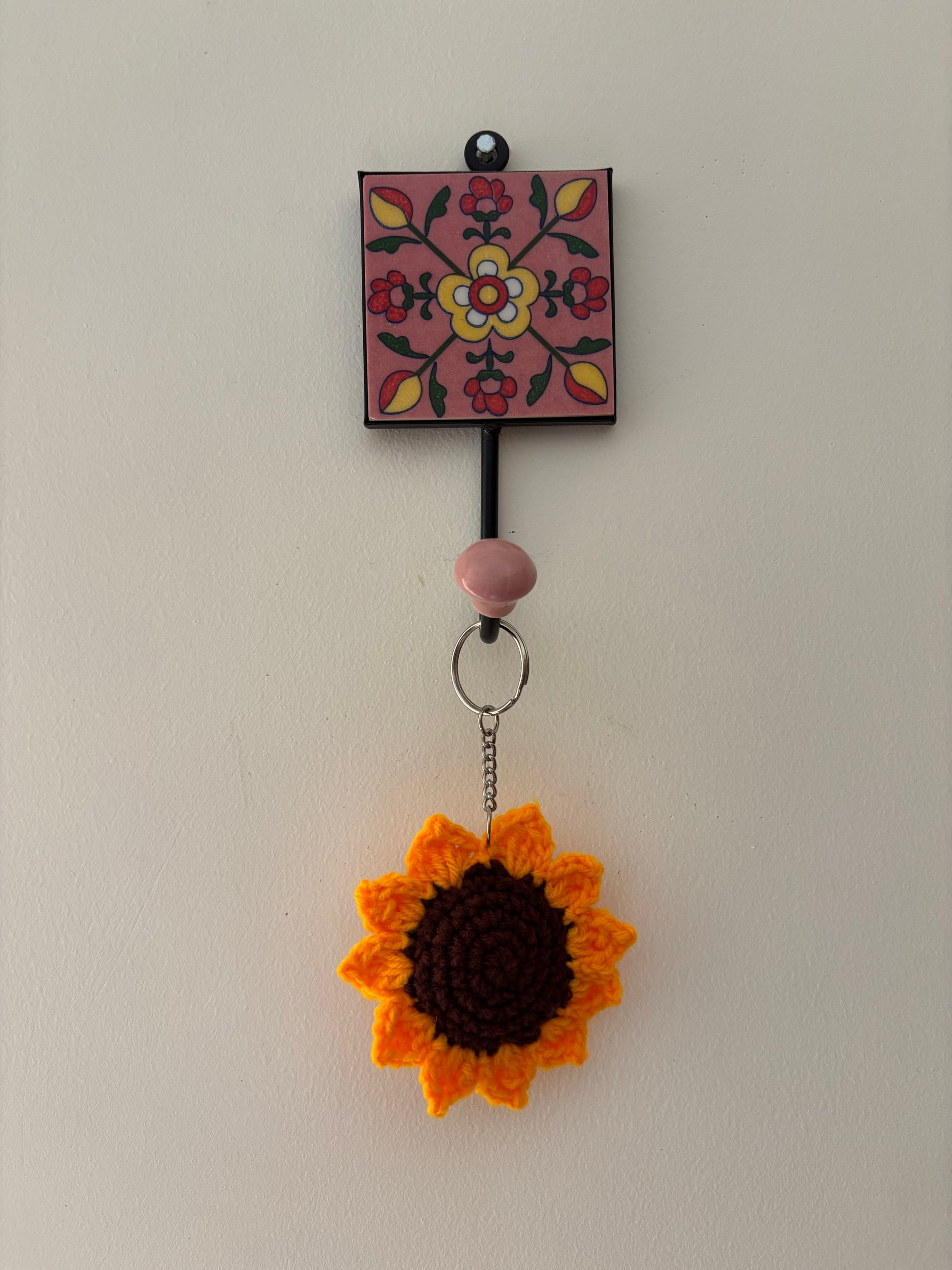Crocheted sunflower keychain attached to a decorative wall hook with floral design.
