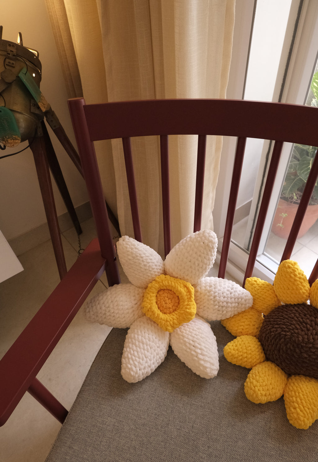Handmade crocheted flower-shaped cushions in a home setting, featuring a white daisy with a yellow center and a yellow and brown sunflower.