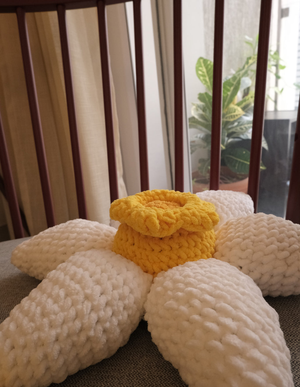 Handmade crocheted flower-shaped cushions in a home setting, featuring a white daisy with a yellow center closeup