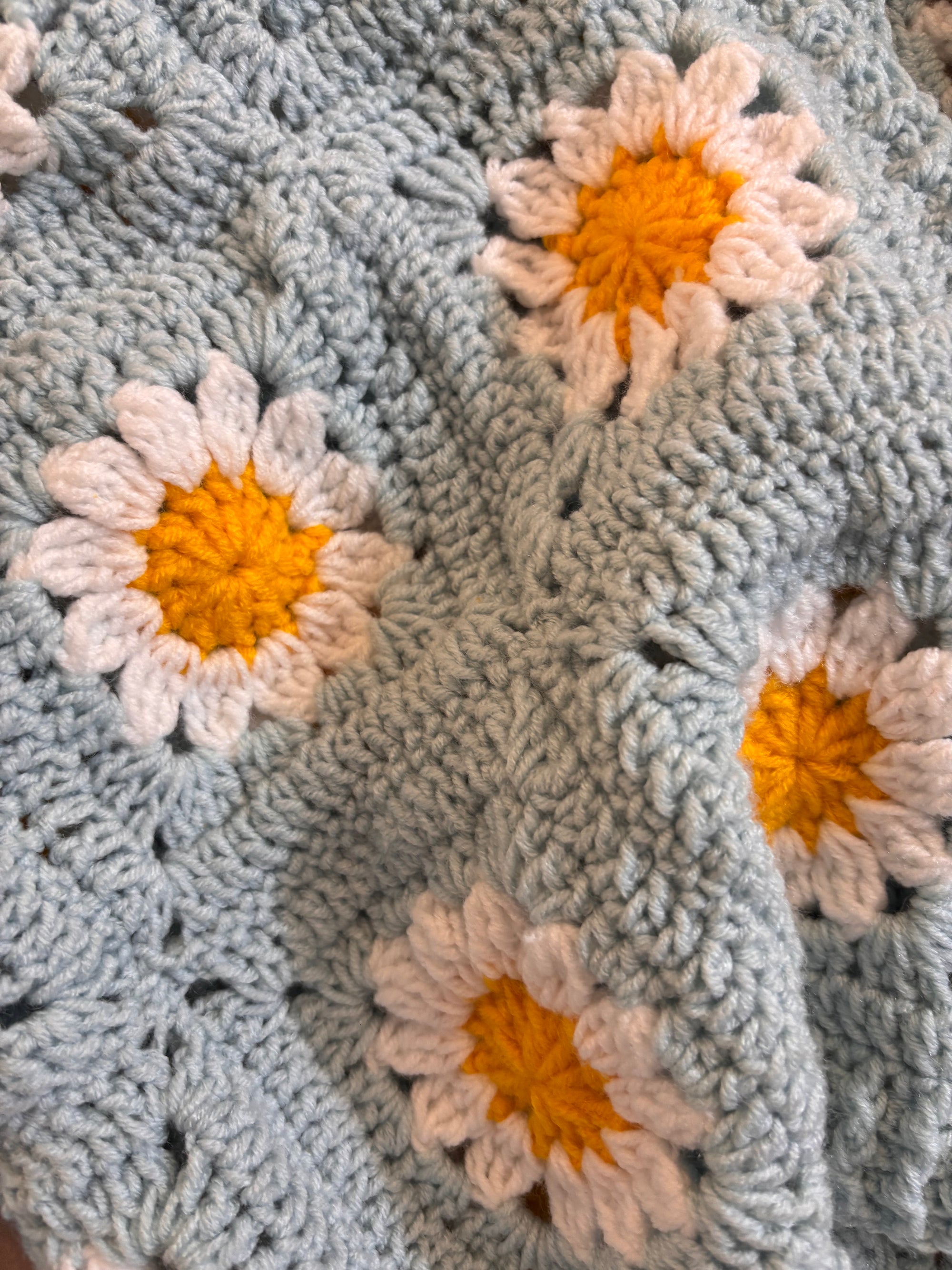 Crocheted cardigan with flower patterns featuring orange centers and white petals.