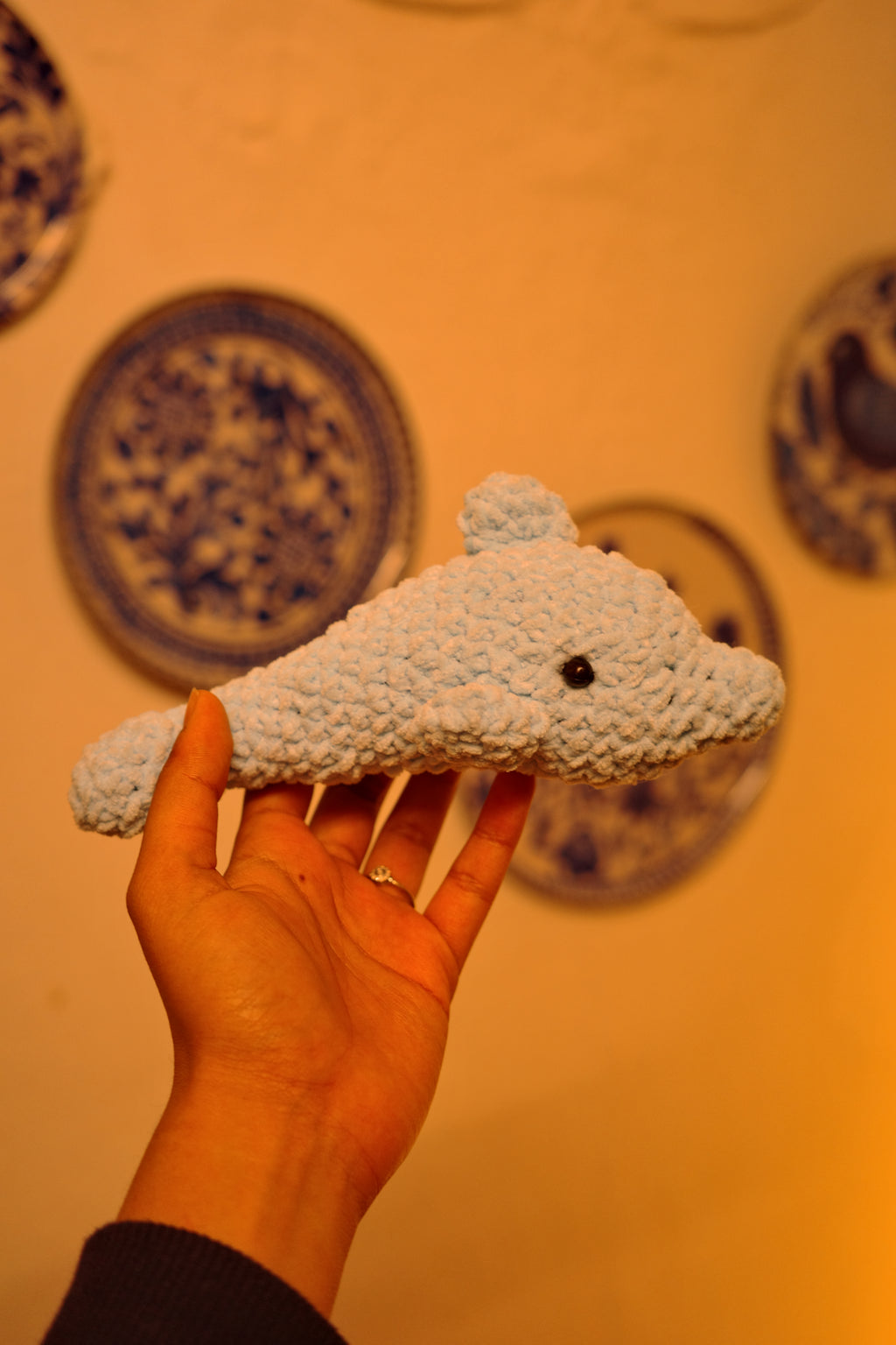 Hand holding a textured plush toy against a decorative wall with blue patterns.