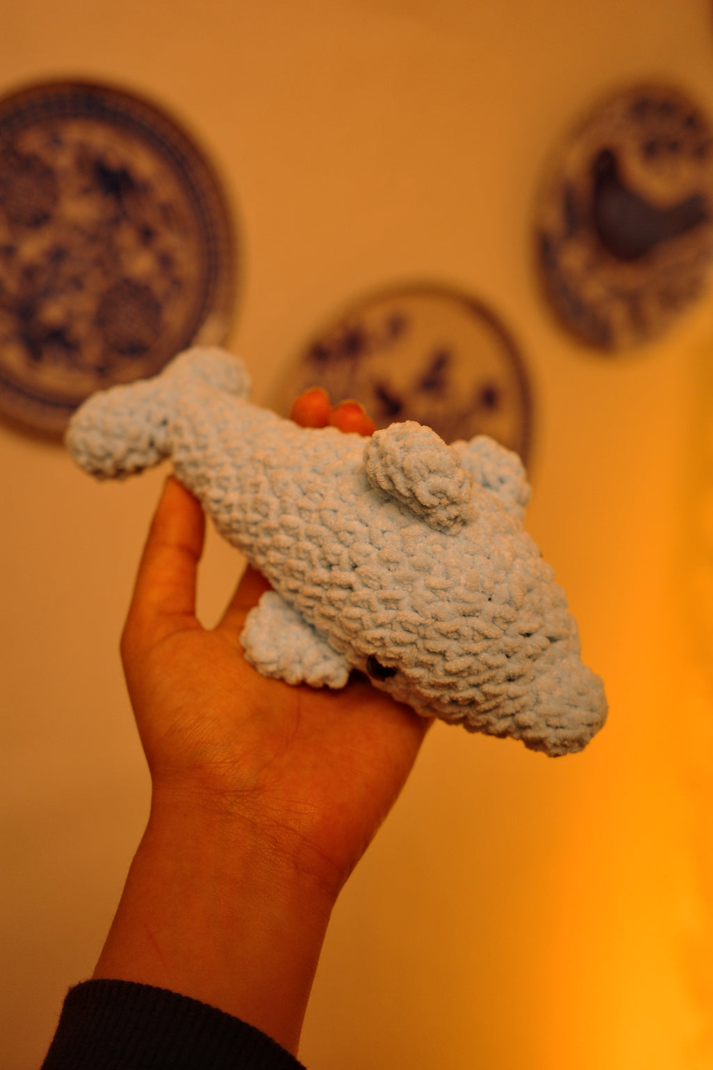 Hand holding a textured dolphin amigurami toy against a blurred background