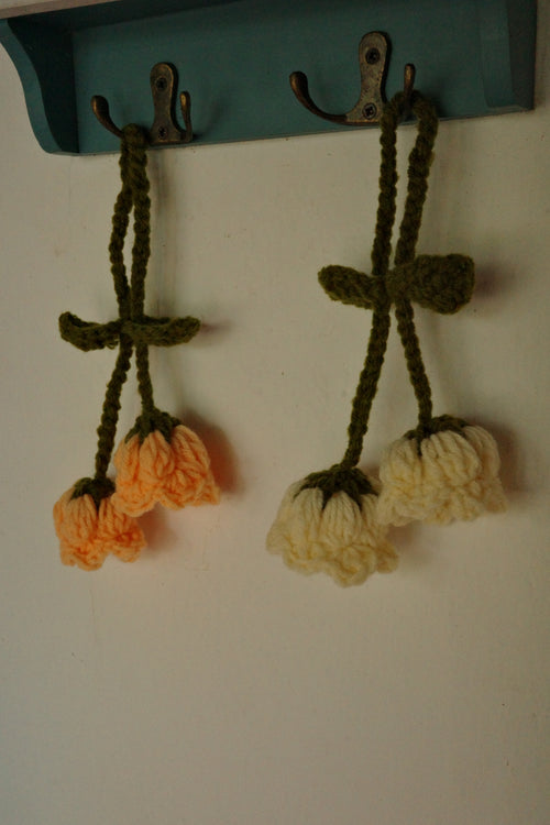 Two crocheted flower decorations on a white surface with a teal object in the corner.