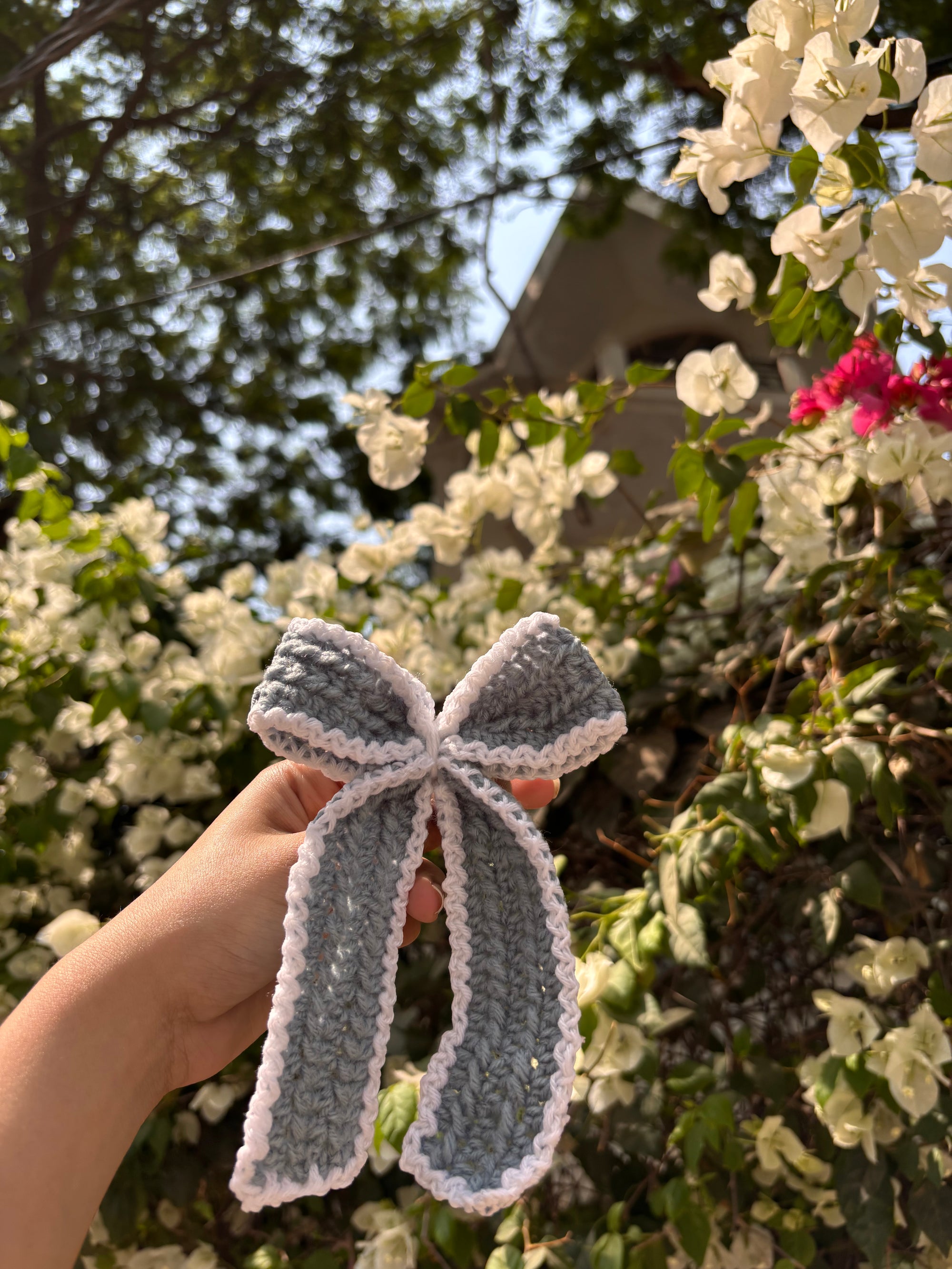 Hand holding a gray knitted bow against a floral background