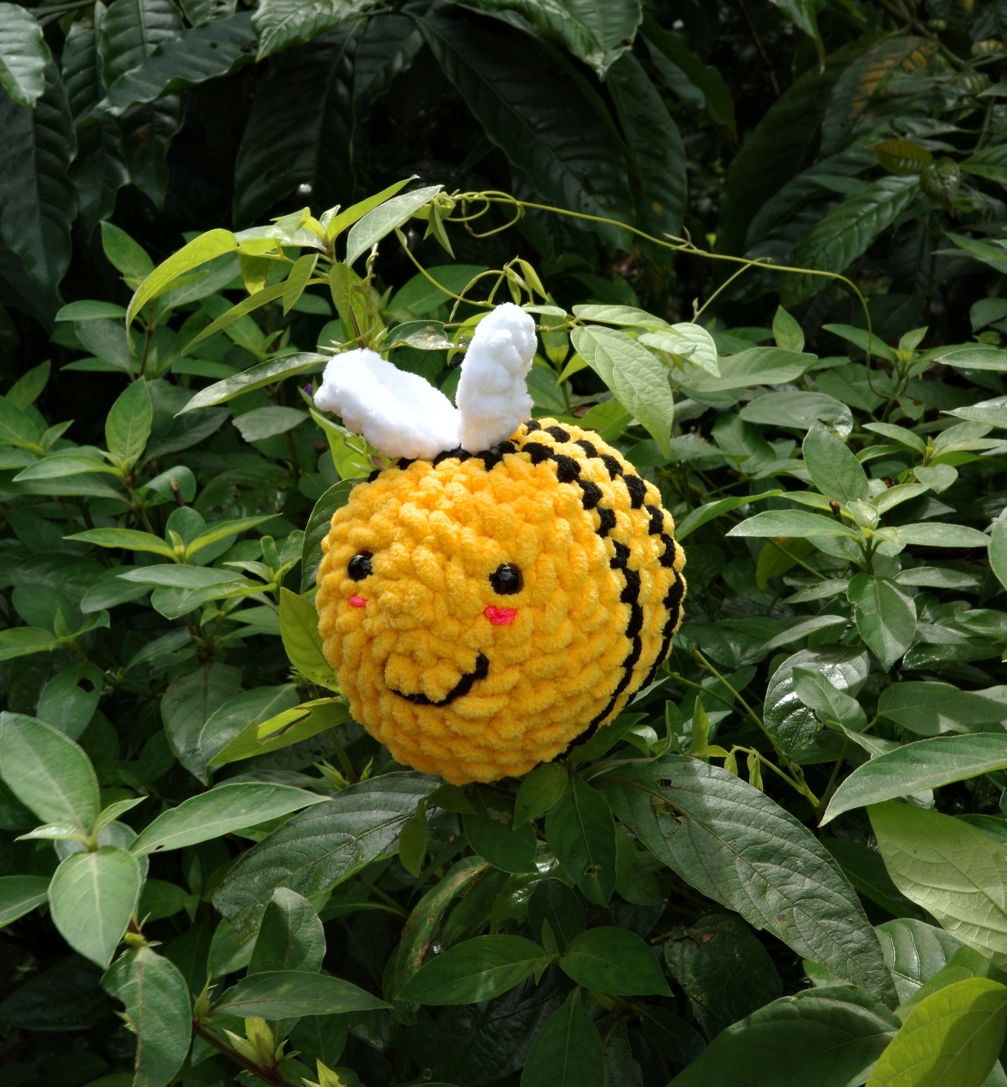 Crocheted bee toy with a smiling face on a green leafy background