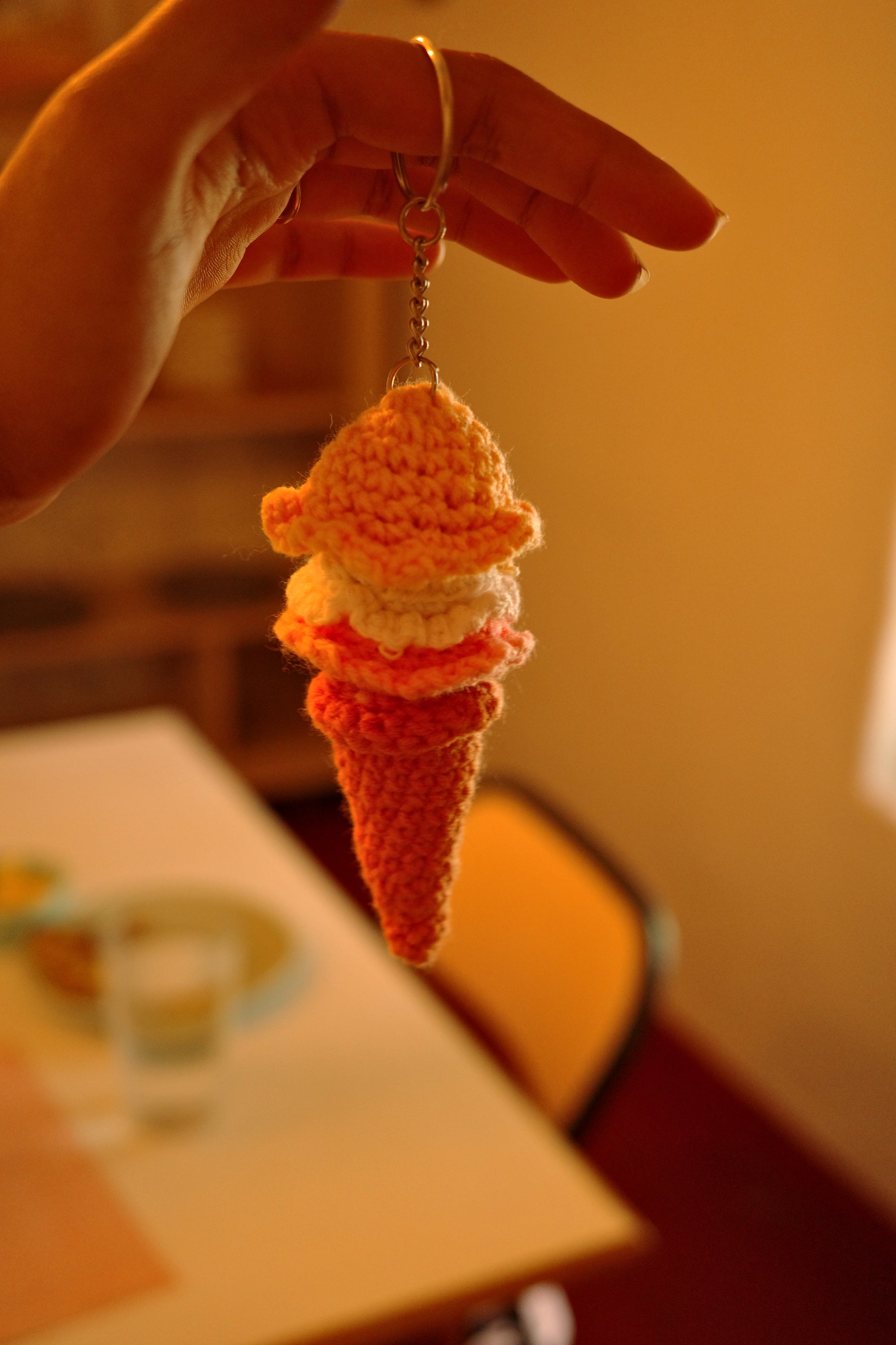 Hand holding a small crocheted ice cream cone with a blurred background
