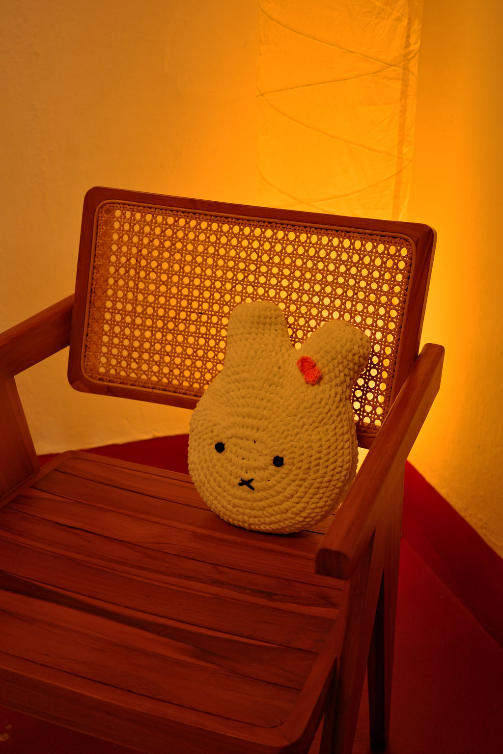 Small knitted miffy cushion toy on a wicker chair with a warm glow