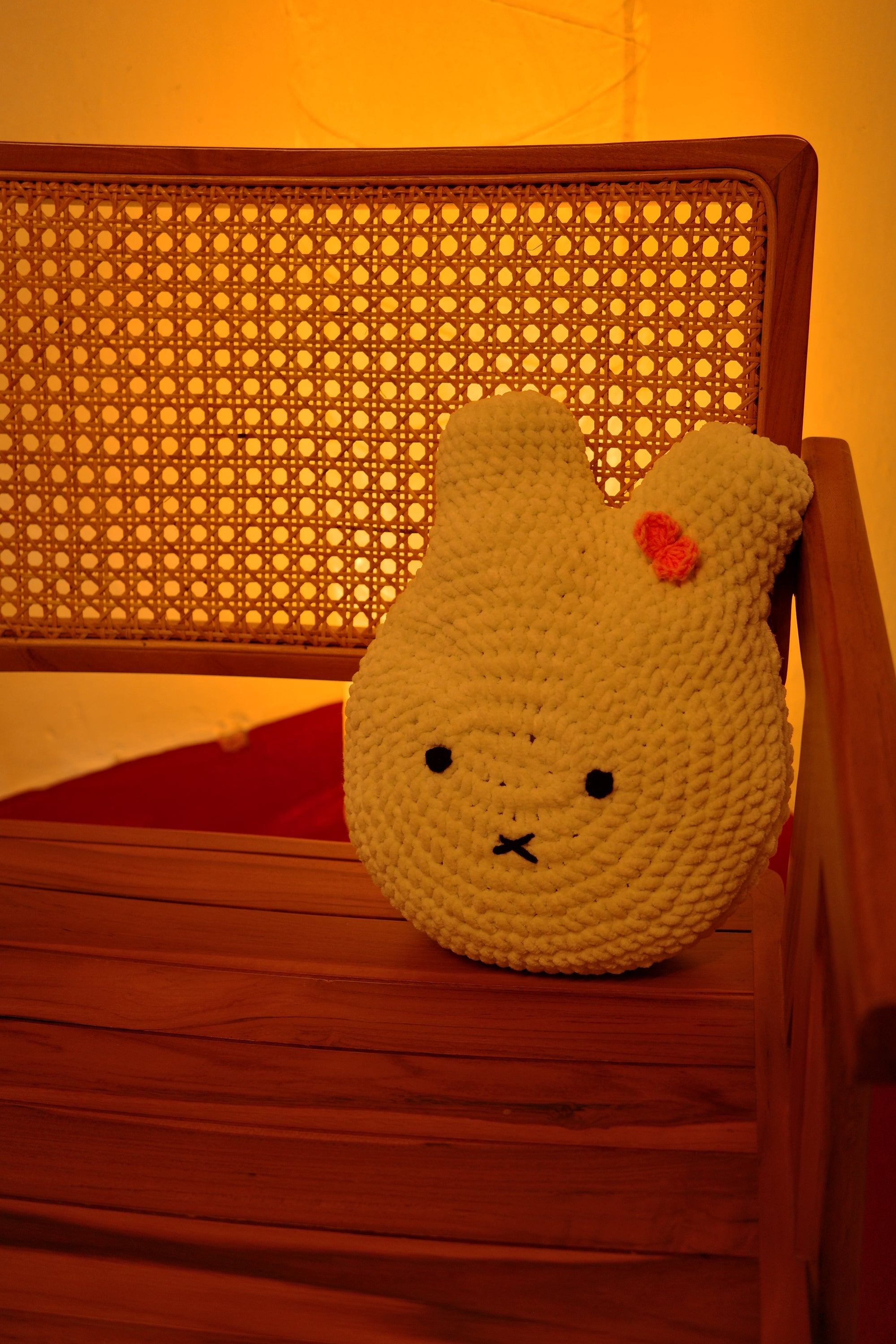 Crocheted miffy cloud-shaped pillow with a face on a wooden surface with a warm glow.