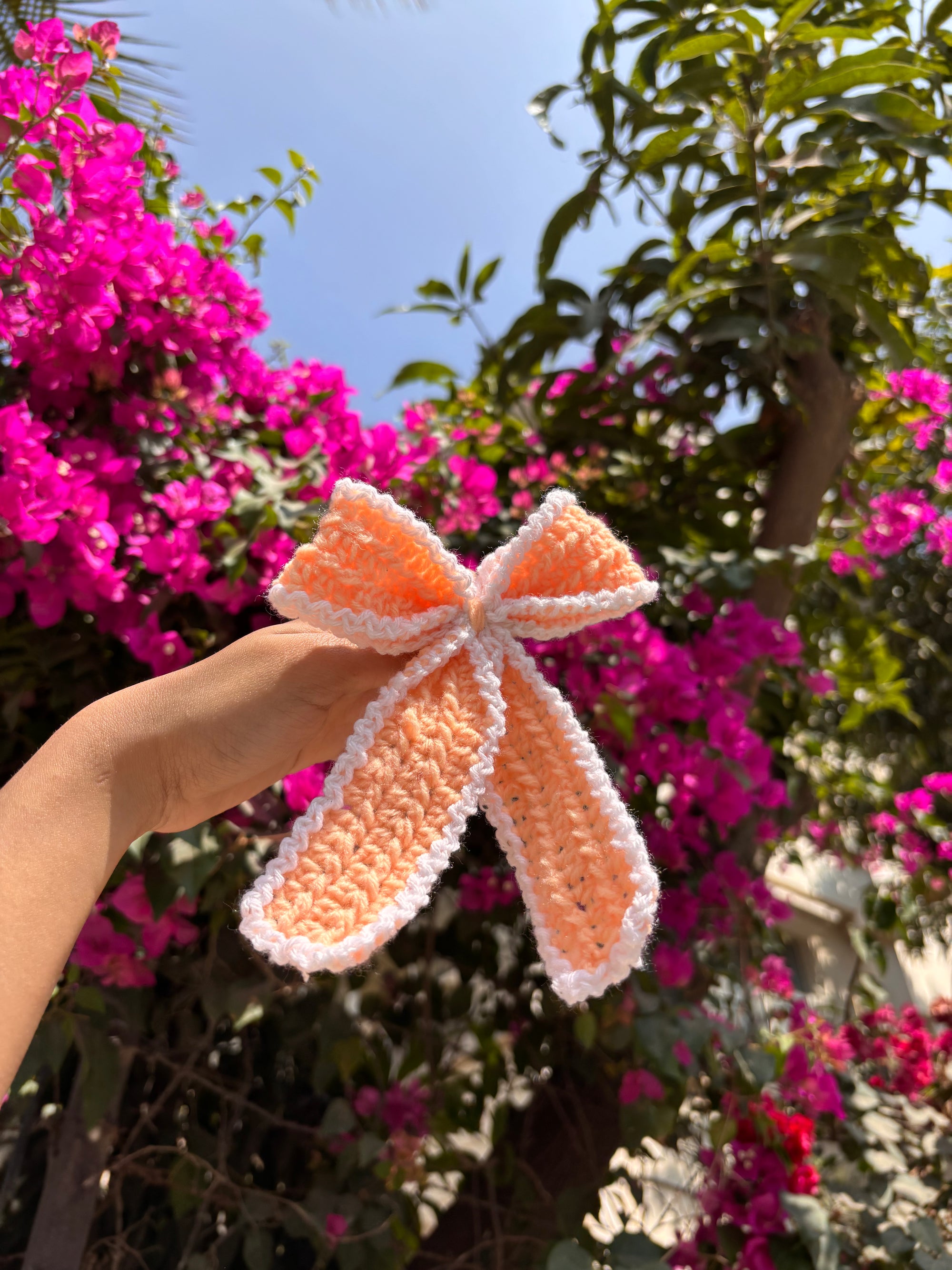 Hand holding a crocheted bow with pink flowers in the background