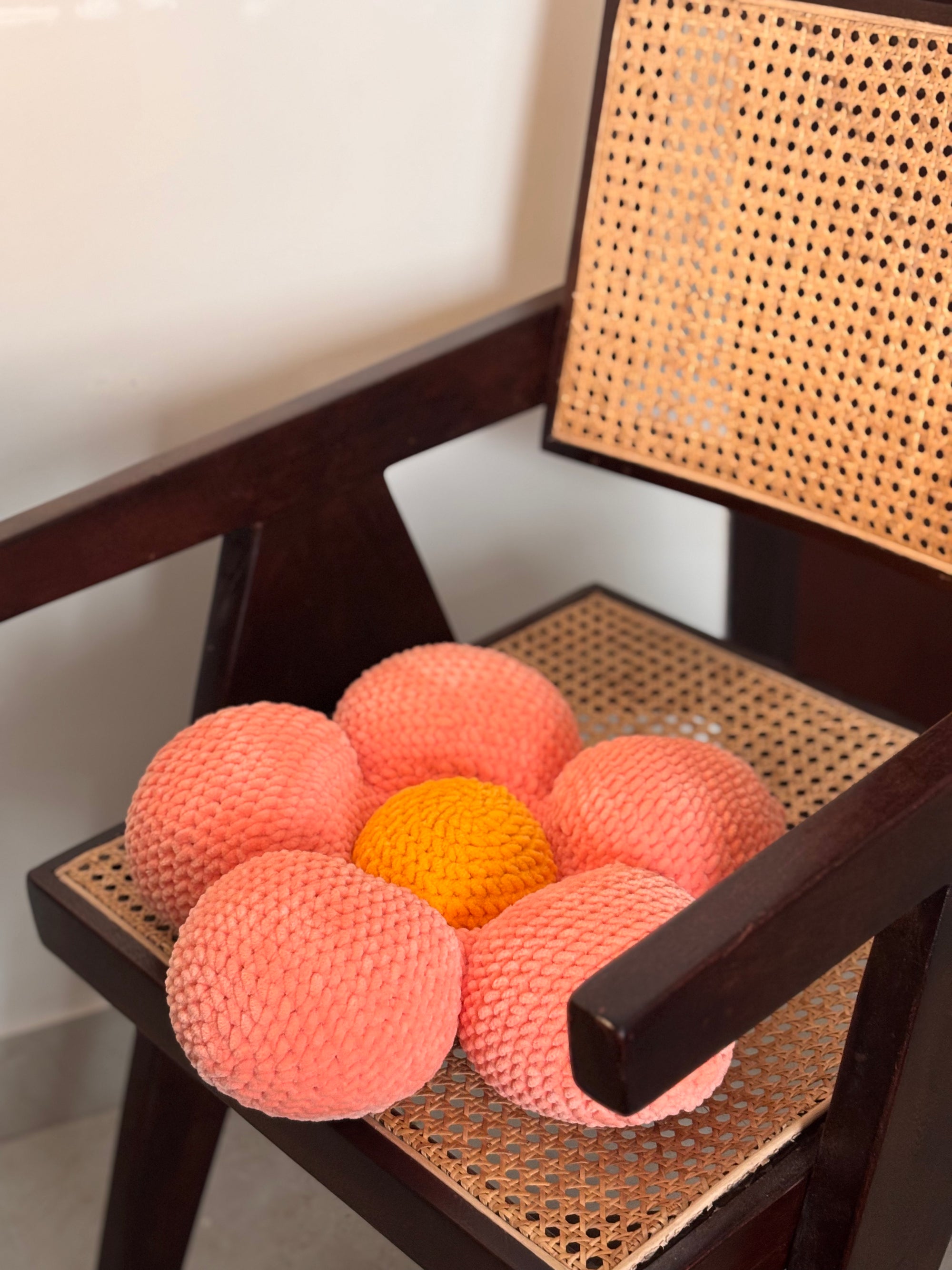 handmade crochet peach flower cushion with rounded petals and yellow center placed on a wooden chair