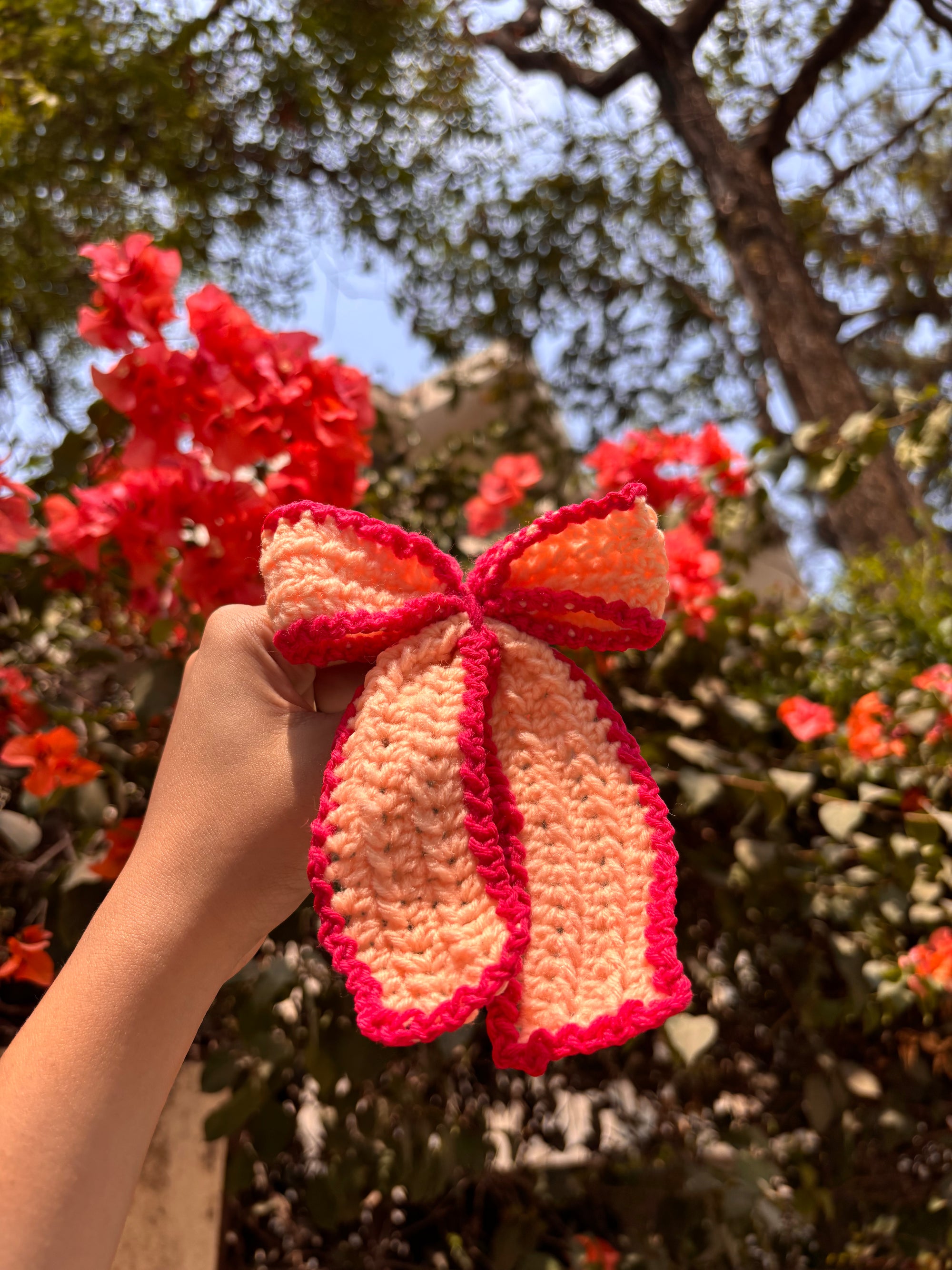 Hand holding a crocheted bow with a floral background