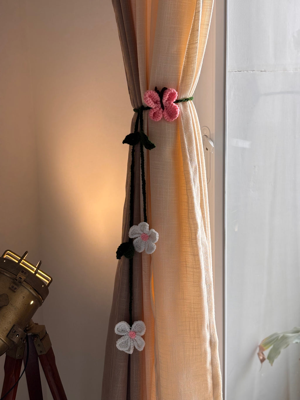 Decorative floral crochet curtain tiebacks on a beige curtain with a neutral background.