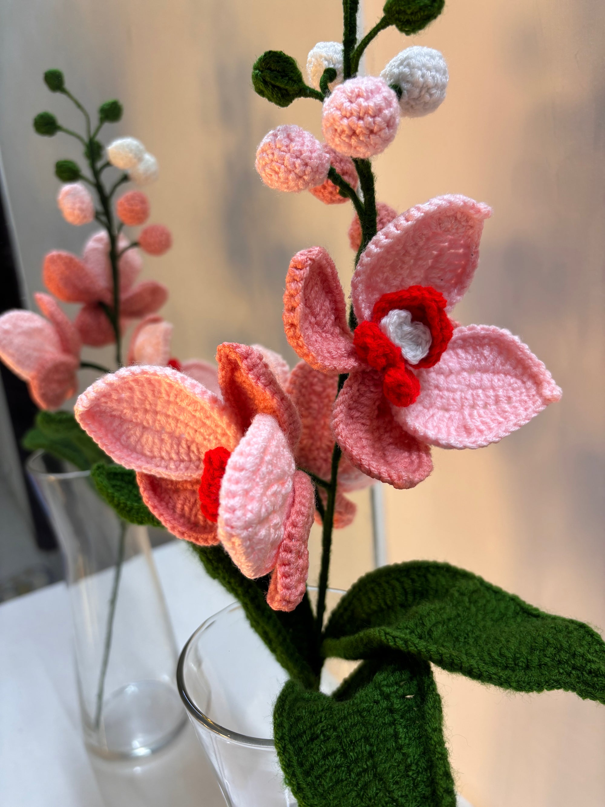 Handmade crochet orchid stem with soft pink flowers, green leaves, and tiny buds 