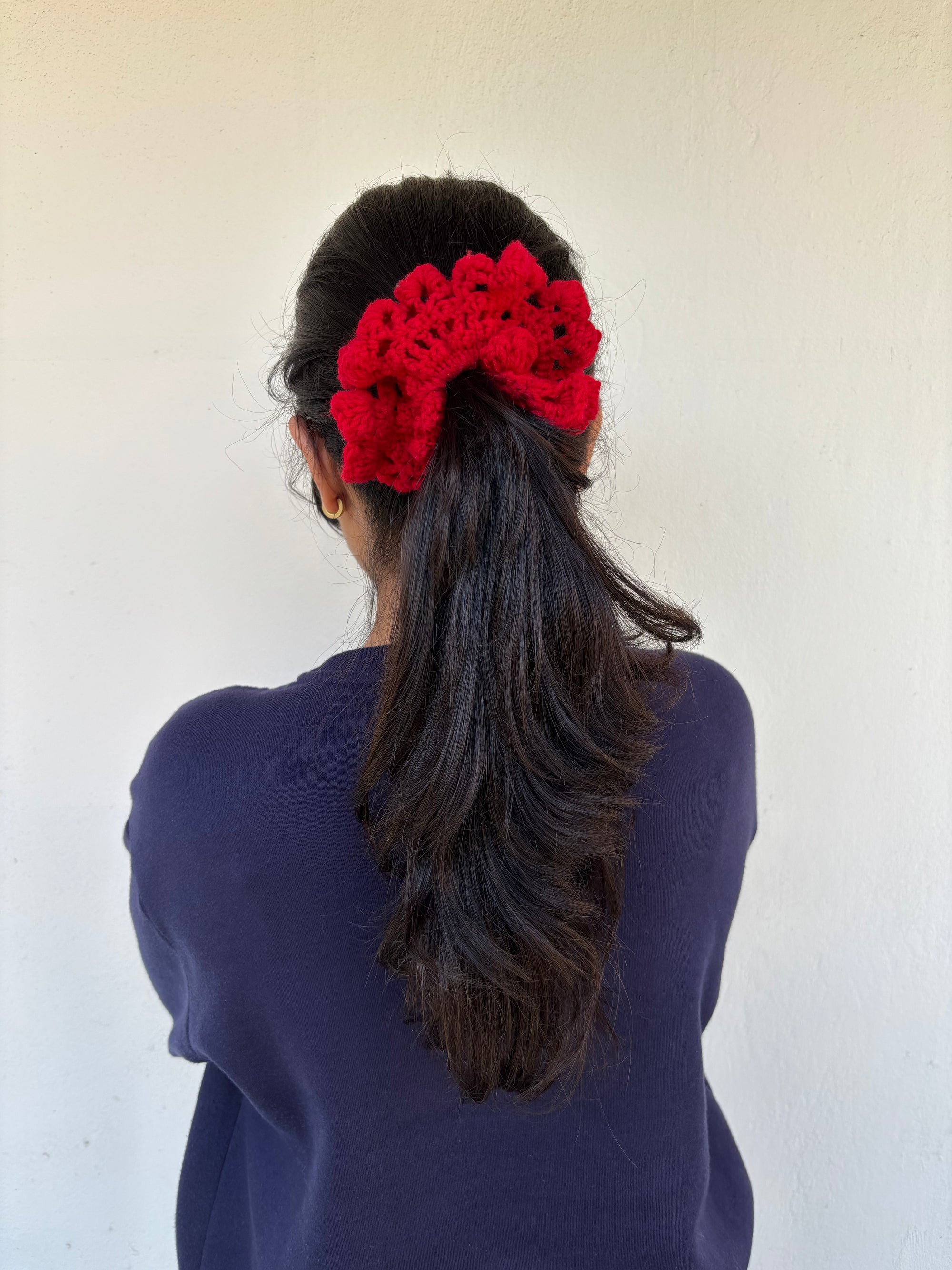 Person with a red crochet hair scrunchie accessory in their ponytail against a white background
