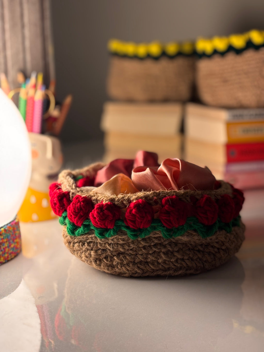 handmade round jute basket with red crochet flower border and green trim, rustic decorative storage bowl for desk or shelf