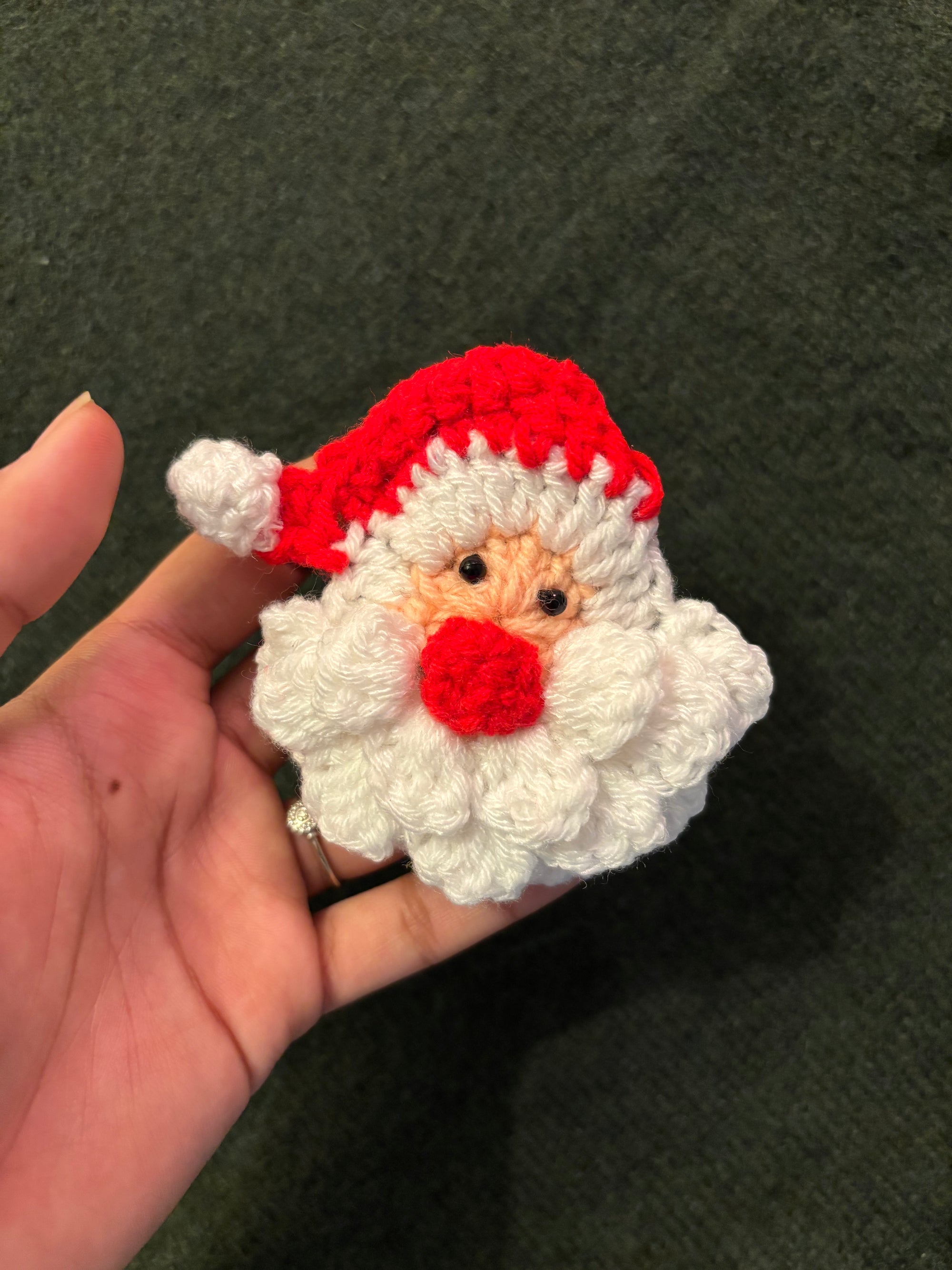 Hand holding a small crochet Santa Claus figure against a dark background