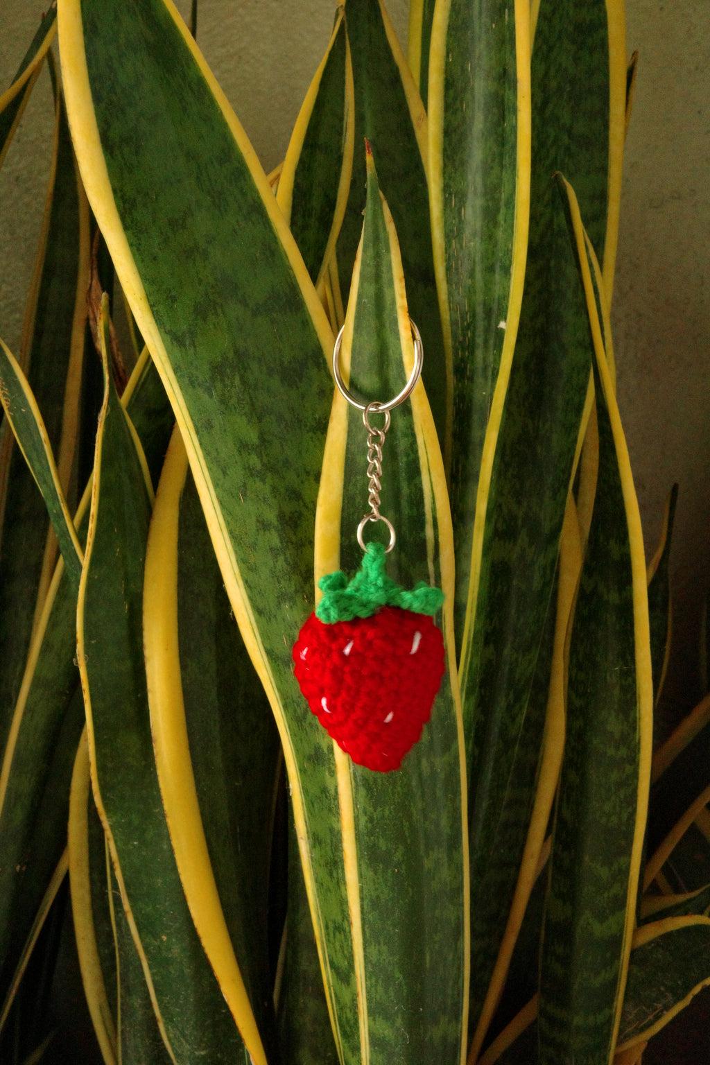 Crocheted strawberry keychain on a leafy background