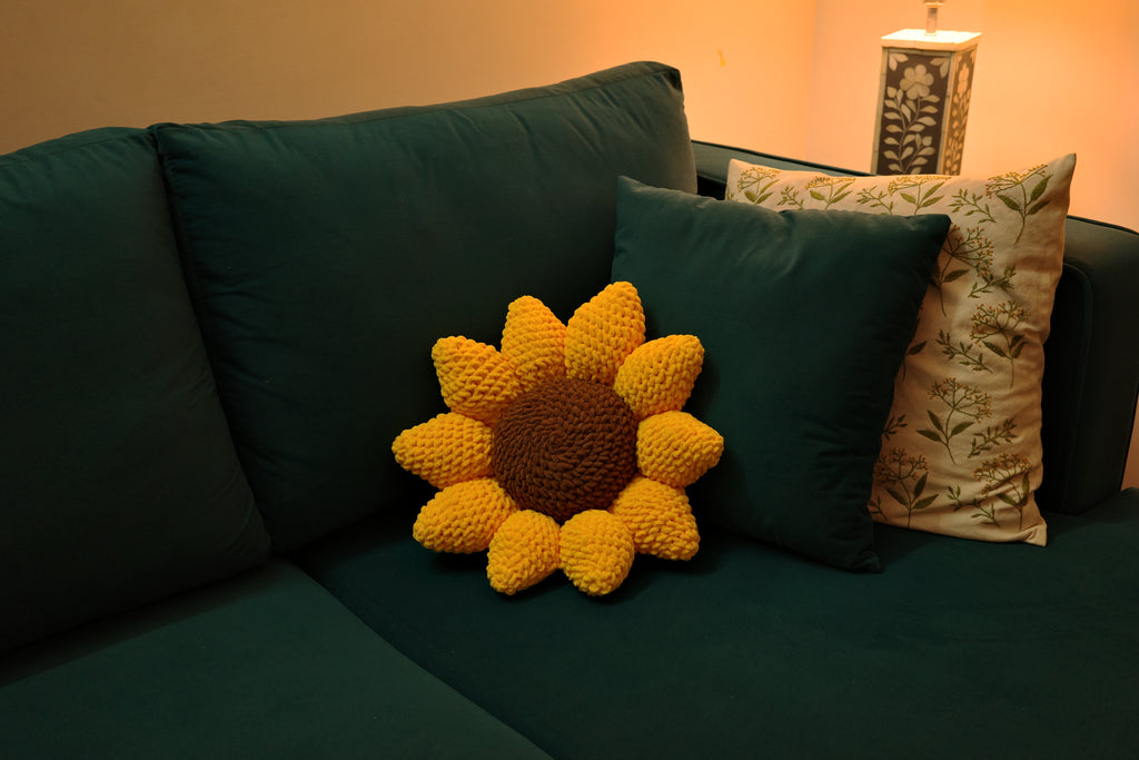 Green sofa with a sunflower-shaped pillow and a patterned pillow on a neutral background