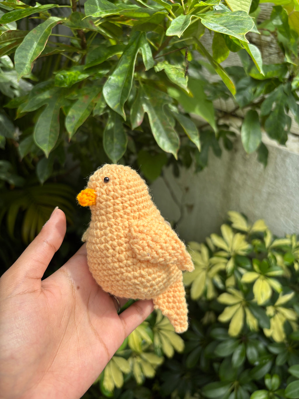 Hand holding a small crochet bird in front of green foliage