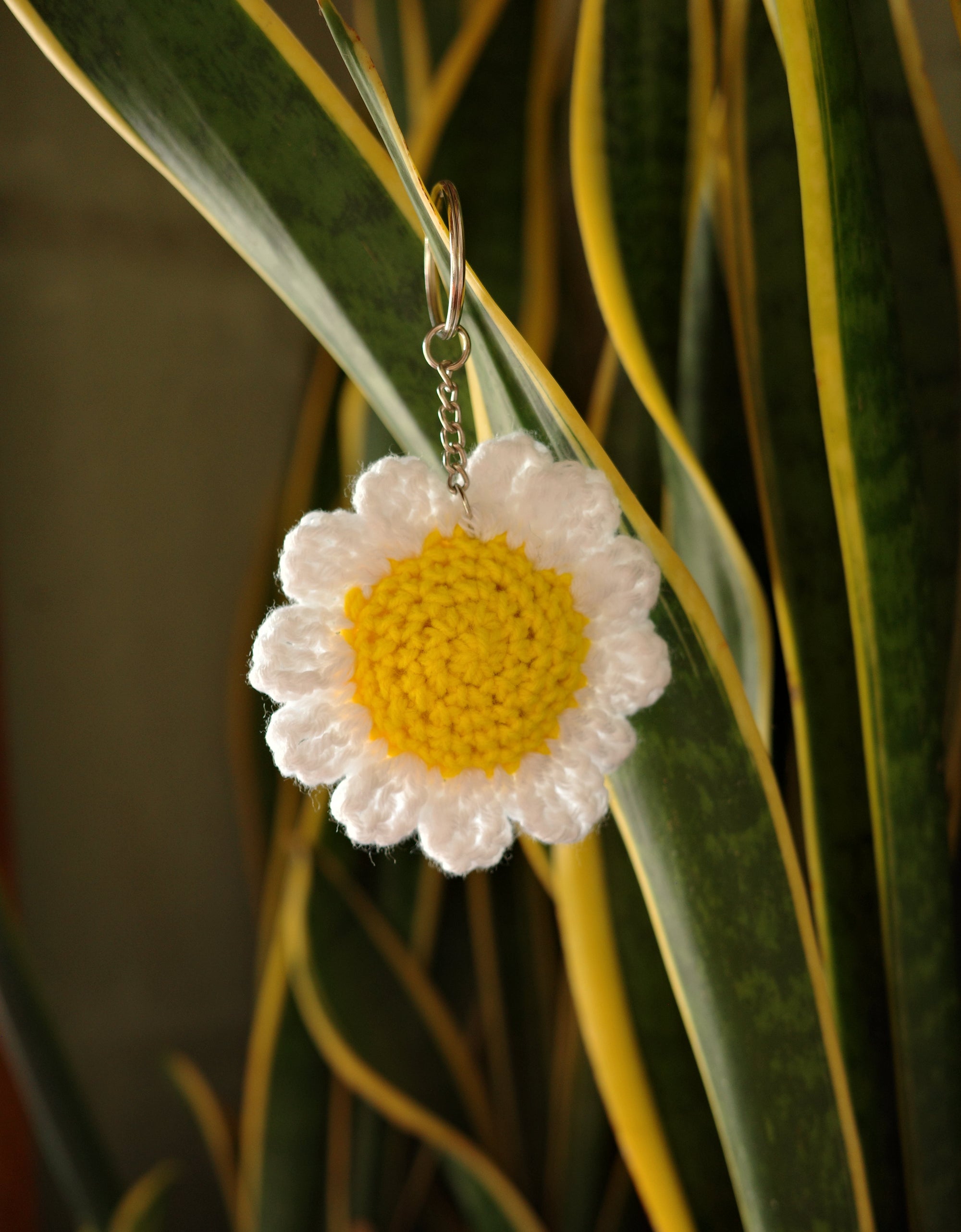 Crocheted daisy flower keychain on green leaves